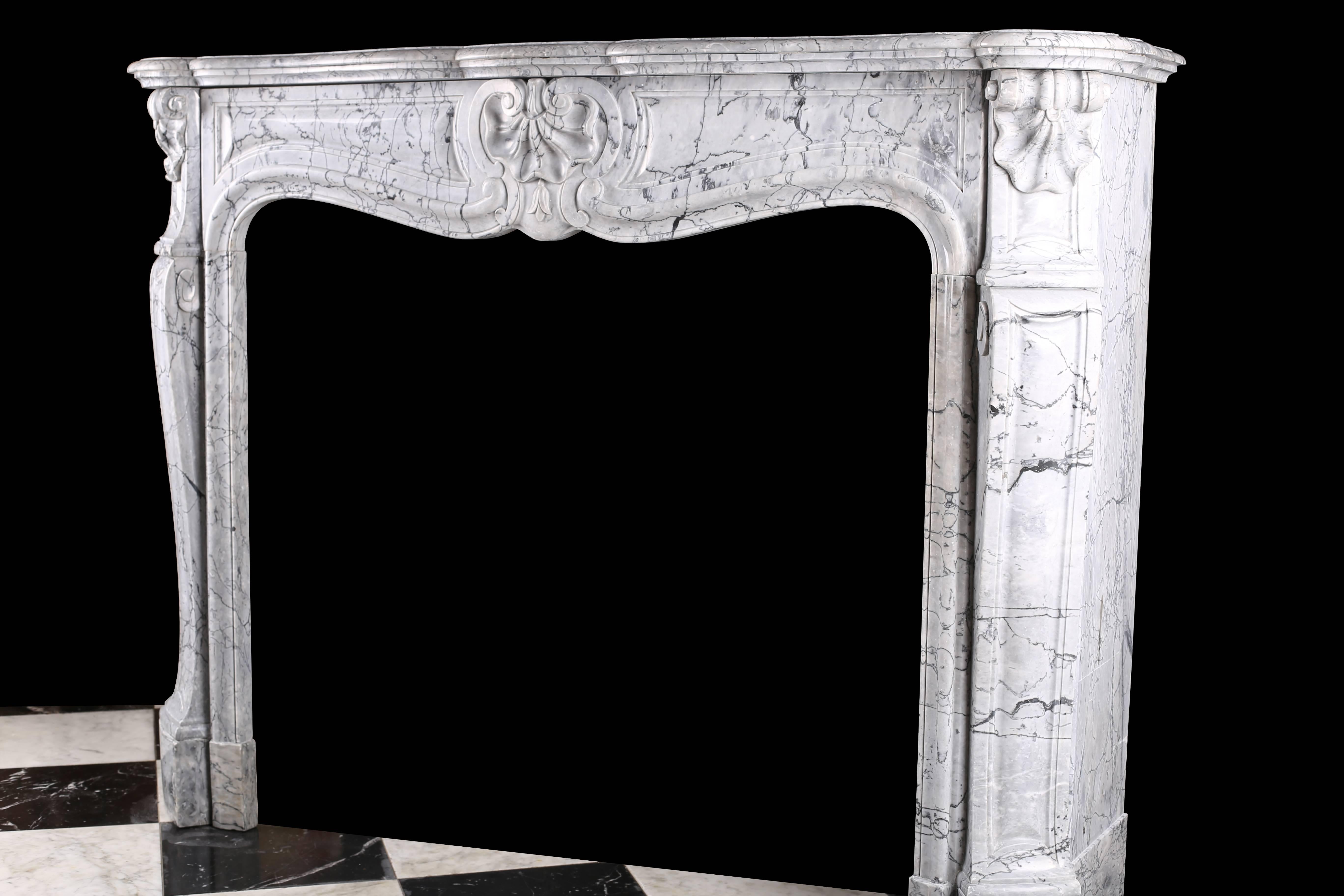 An antique Louis XV Rococo fireplace mantel very finely carved in elegantly veined Italian Bardiglio black veined blue grey marble, with a serpentine shelf over the finely carved panelled frieze with a central shell cartouche and with very