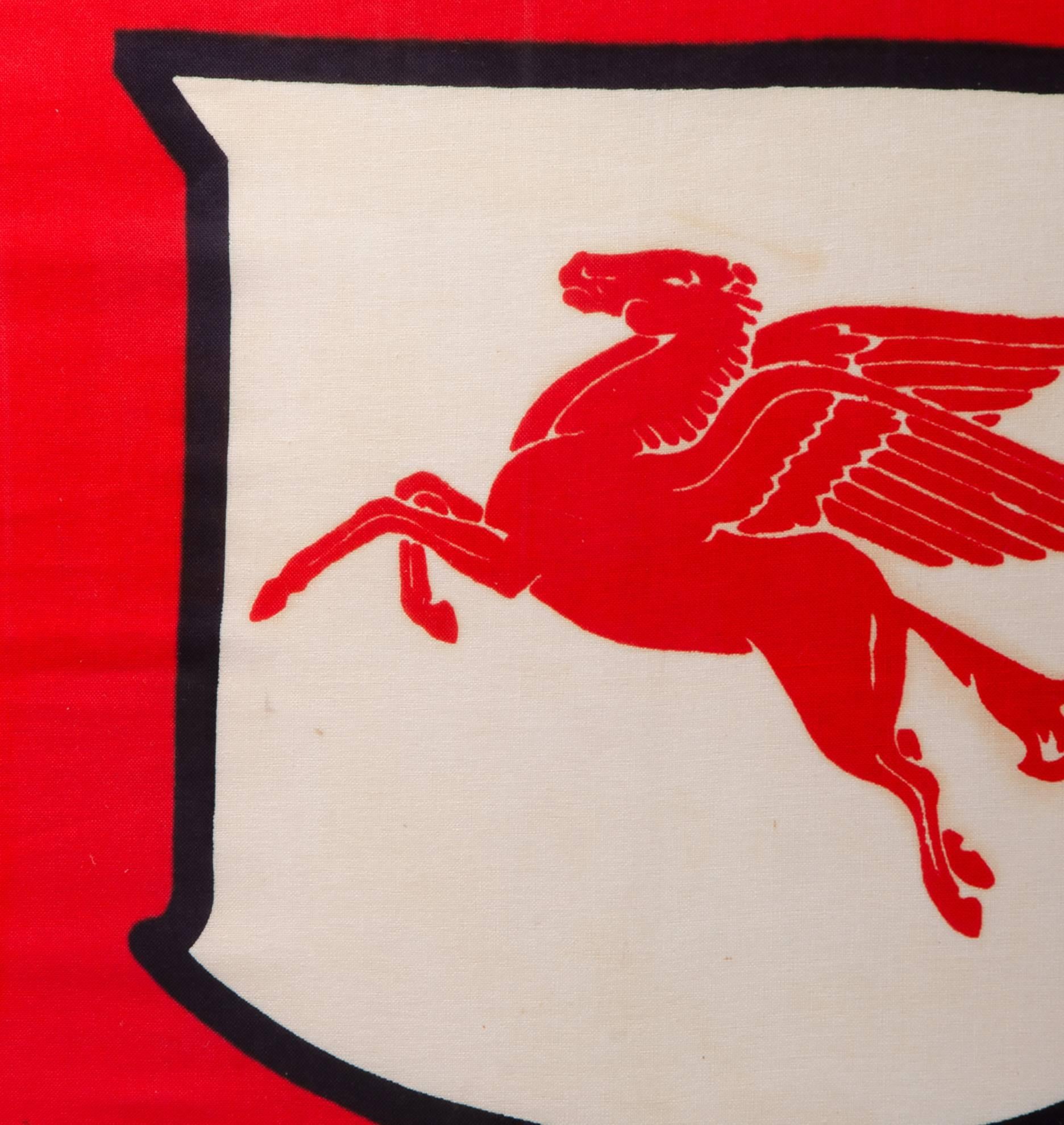 An incredible relic from a Mid-Century raceway, this Mobil gas flag depicts the iconic Pegasus on a shield over a bright red background. The pattern appears to be screen printed, with very little bleed between the colors.