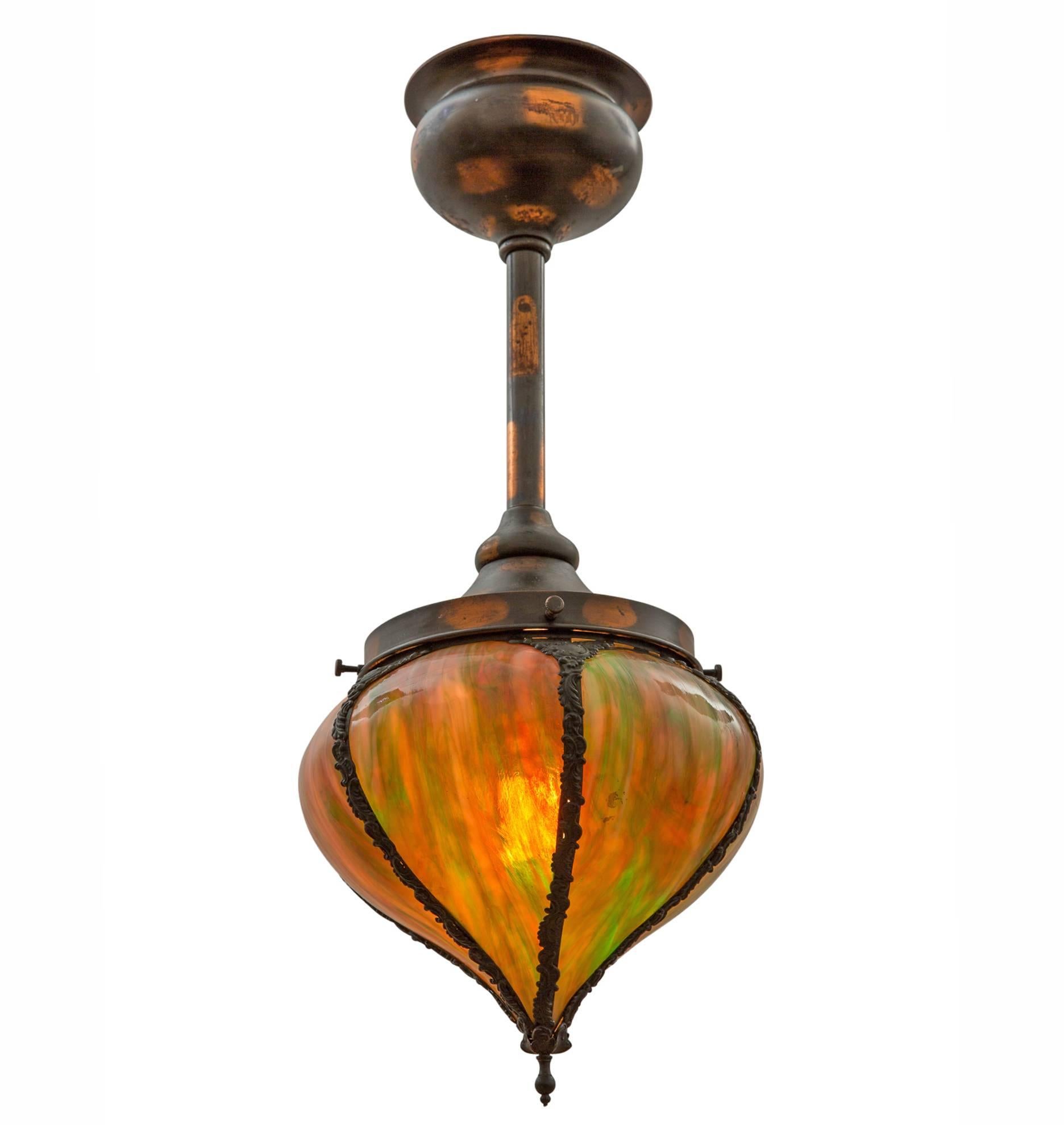 A rare jewel: an early electric Victorian pendant, complete with japanned copper finish and an enormous five-paneled art glass shade. The shade, which bulges like an onion dome, is adorned with brass straps, cast with incredibly ornate patterns.