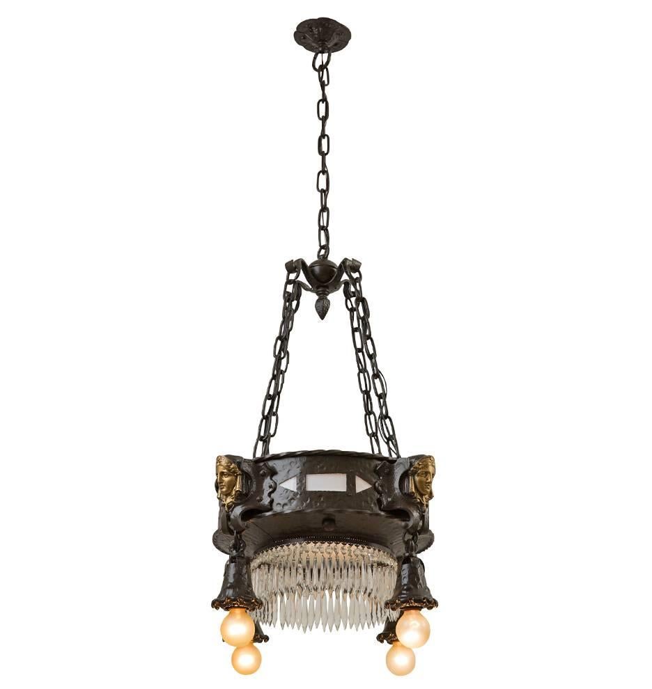 Where the Romance Revival movement is concerned, more is often more. This incredible chandelier does not disappoint: the wrought style drum features panels of milk glass, a ring of crystal spears, four bare-bulb satellites and four cast female faces