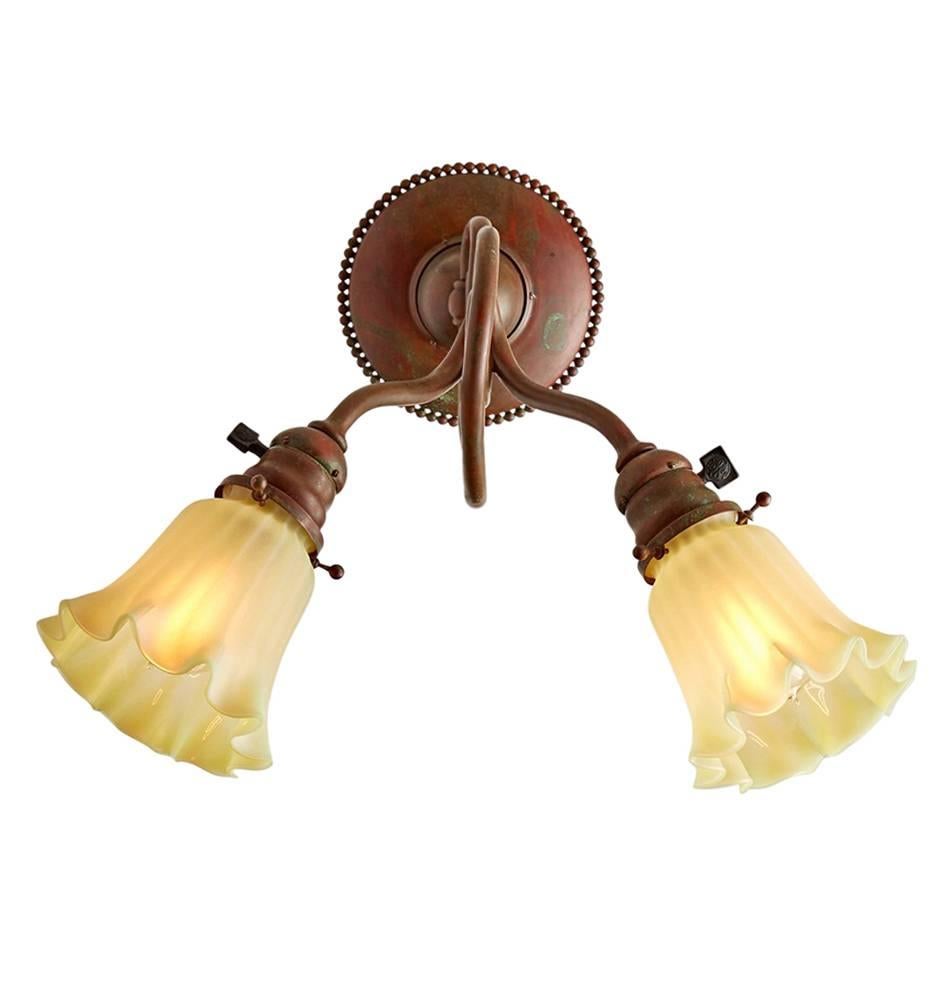 Shown here is a pair of Tiffany Studios wall sconces, combining a pair of turn-of-the-century Tiffany Metalware copper brackets with satin-finished Tiffany Art Glass shades. The shades are marked with the 