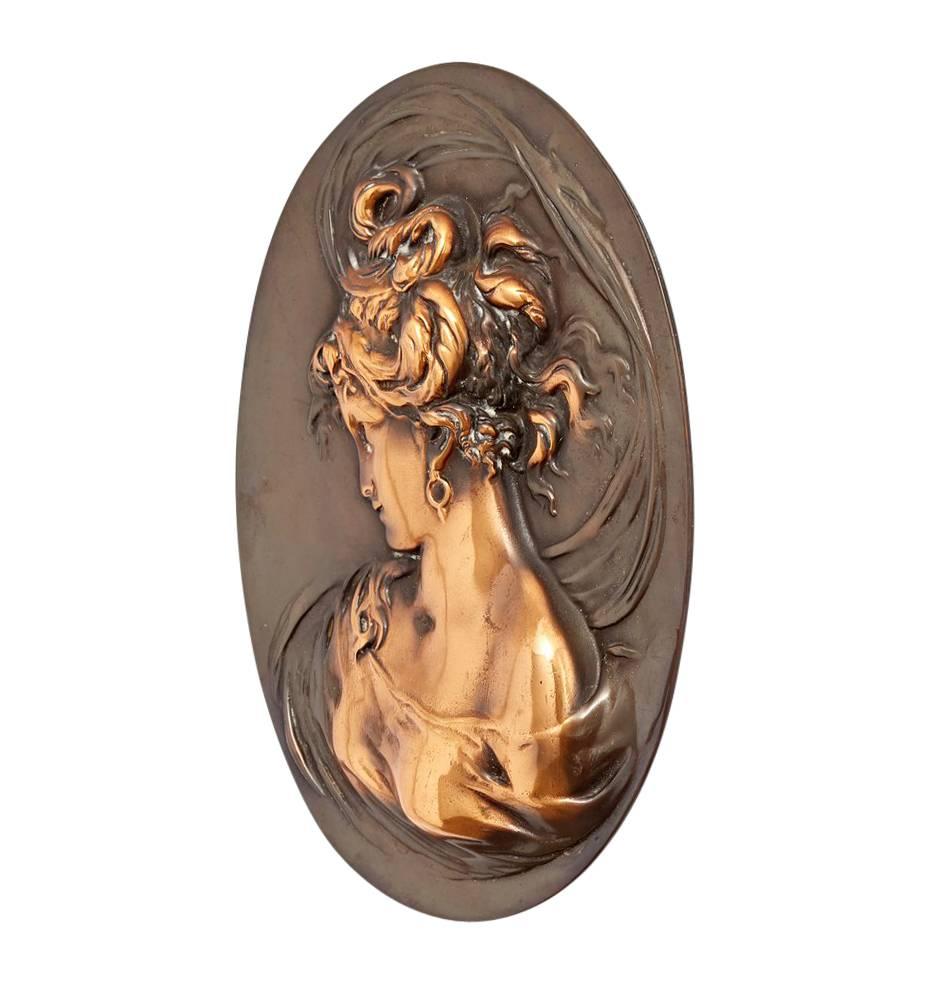 This wonderful example of bas relief metalworking features a beautiful young woman, surrounded in swirling fabrics. The relief stands out against a smooth oval and was perhaps originally incorporated into large furniture piece, mantel or bar back,