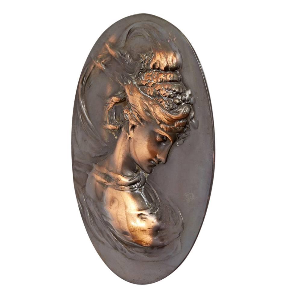 This wonderful example of bas relief metalworking features a beautiful young woman, surrounded in swirling fabrics. The relief stands out against a smooth oval and was perhaps originally incorporated into large furniture piece, mantel or bar back,