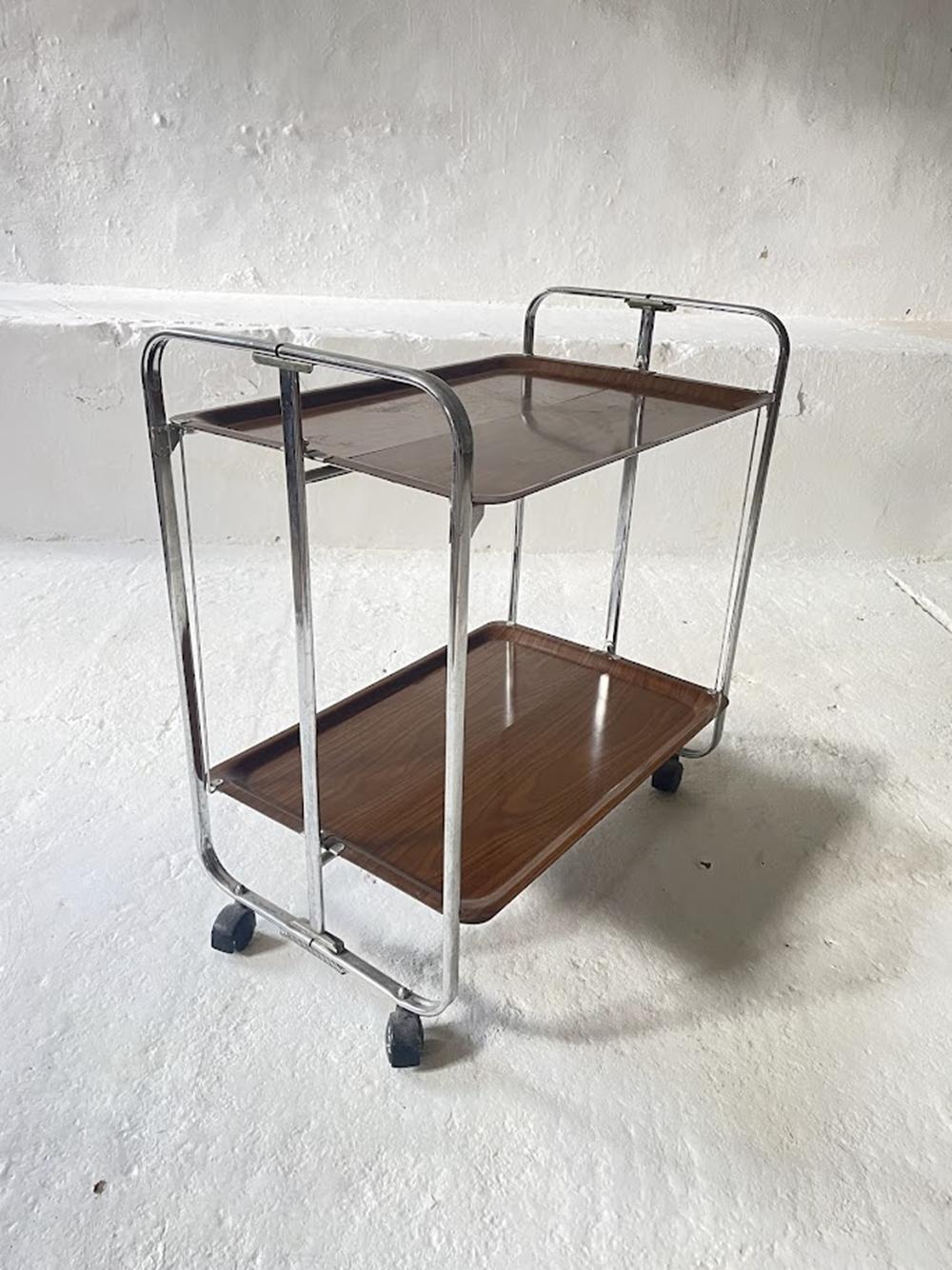 Chariot de service vintage Mid-Century Modern d'Allemagne, datant des années 1950. Ce chariot à thé à deux niveaux, peu encombrant, est fabriqué en bois stratifié et en chrome, capturant parfaitement le design emblématique de l'époque.

Le chariot