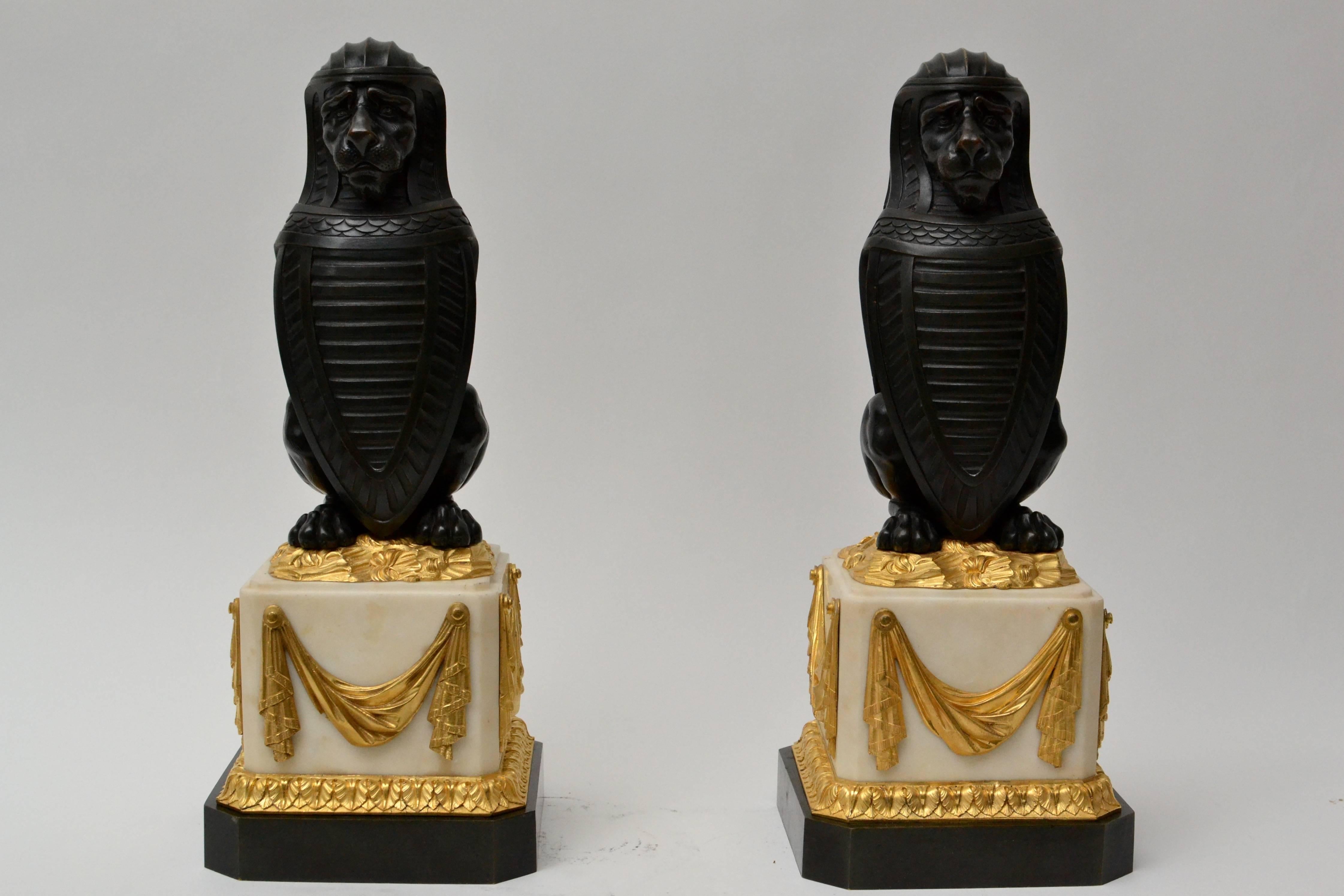 Pair of patinated bronze lions holding a shield on ormolu-mounted white marble bases, probably English, George III and late 18th century.