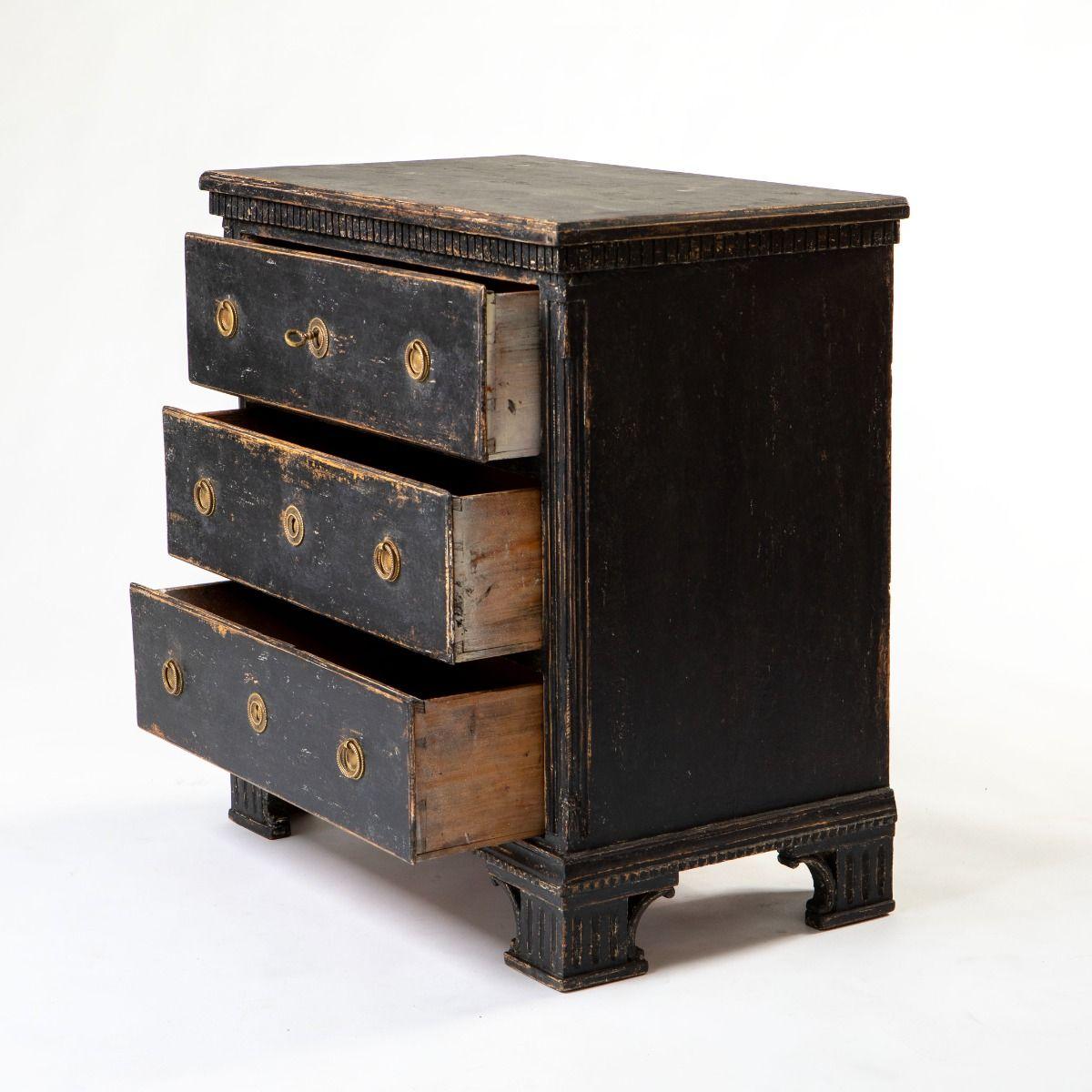 Commode décorative gustavienne (connue au Danemark sous le nom de Louis XVI) fabriquée en pin, soigneusement décapée jusqu'à sa peinture noire d'origine avec une belle patine vieillie.
Le plateau est orné d'une moulure à denticules finement