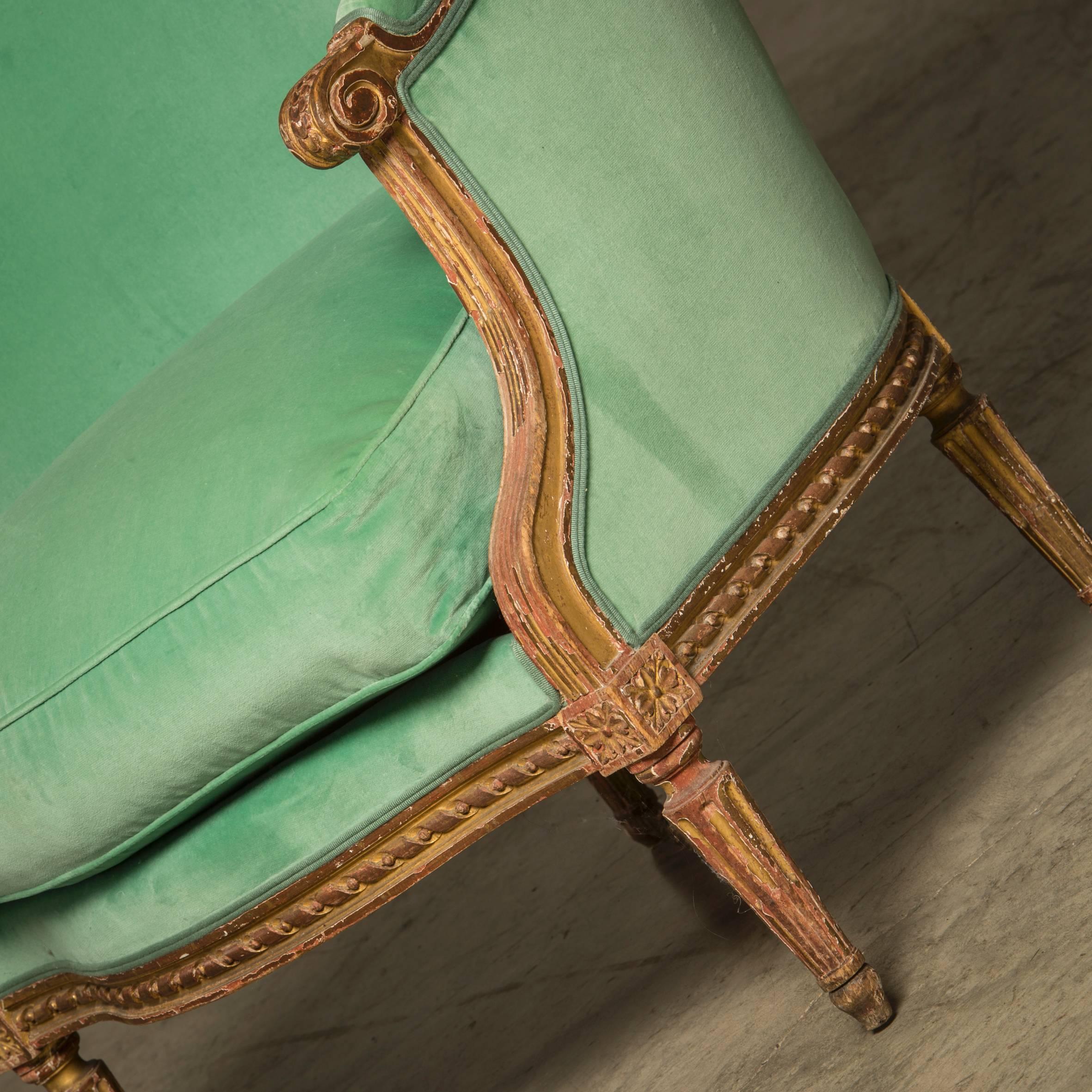 Large French bergere chair in Louis XVI style with matching footstool. Wood carved and gilded. 
France, 1850-1870.
Appears untouched with beautiful patina.

Measurements (cm):
Bergere chair: H 97 /W 75 /d 90.
Footstool: H 30 /W 56 /D 56.