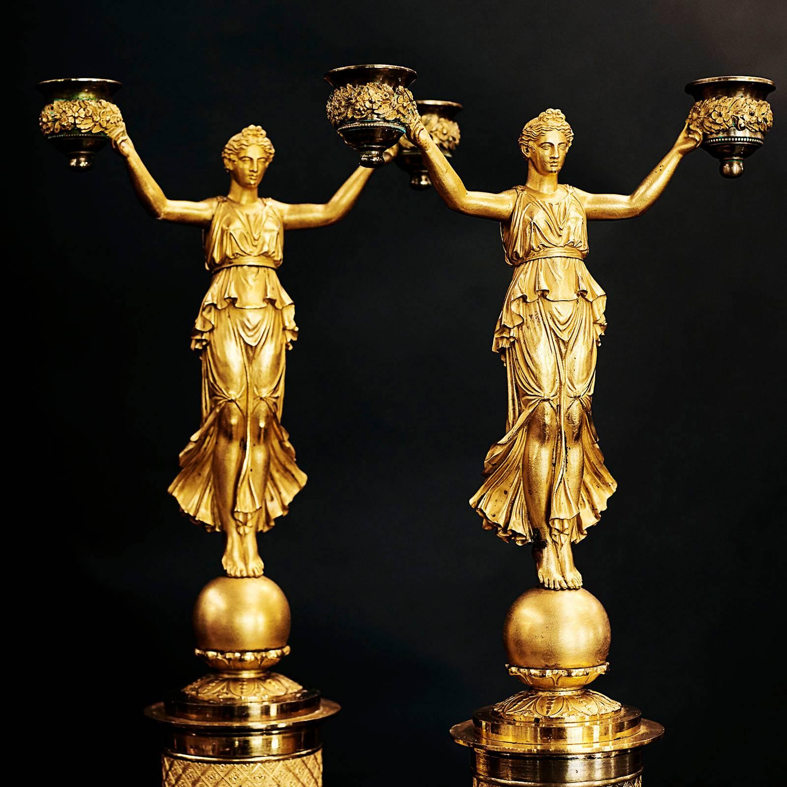 A fine pair of French Empire ormolu candelabra, circa 1810, each with a woman with outstretched arms holding garlands with candle holders, mounted on a sphere and raised on a casts round pedestal with a square plinth base. Superb castings and