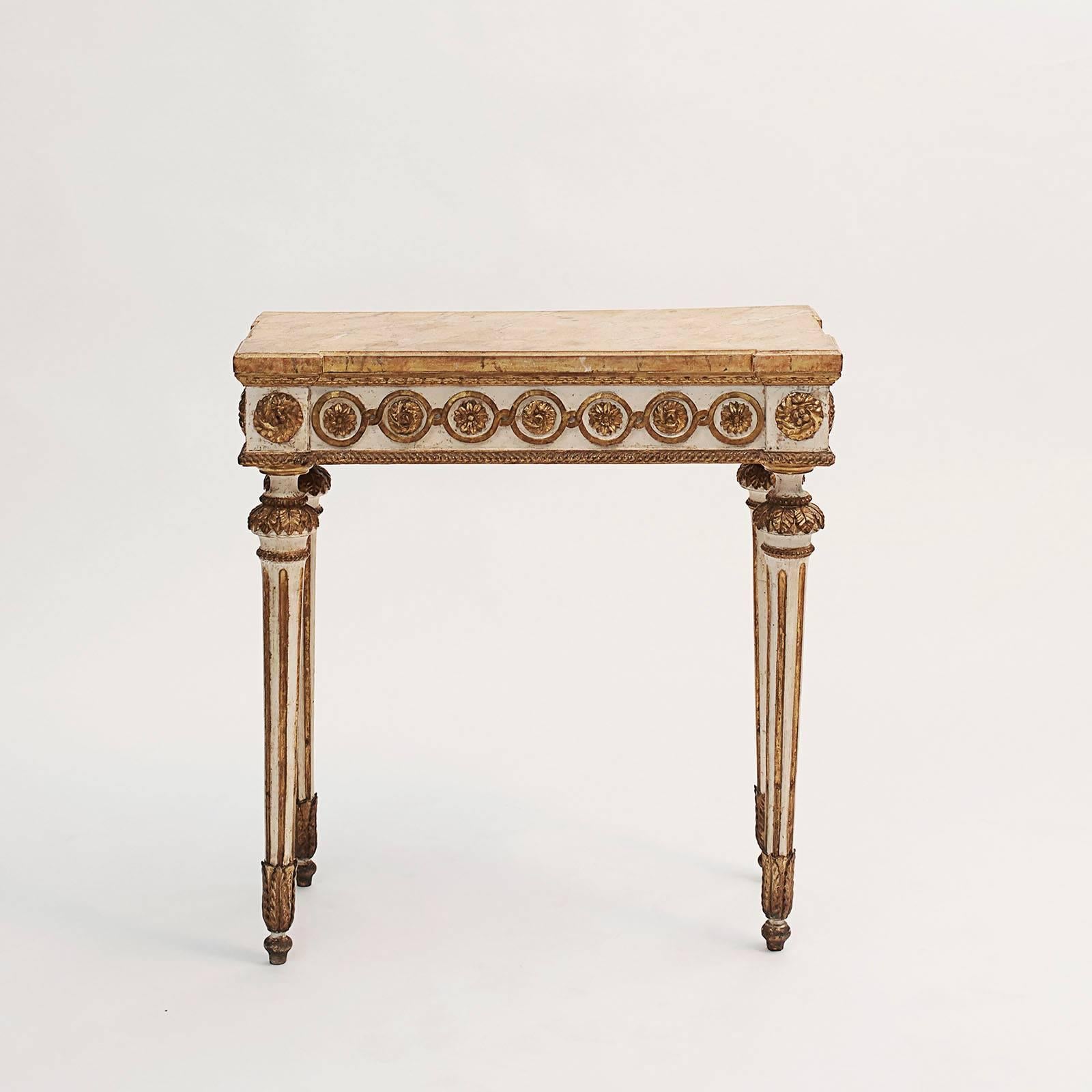 A fine pair of Italian neoclassical carved, painted and gilded consoles, late 18th century. 
The rectangular travertine style painted top with extended corners above a painted frieze decorated with carved circles and rosettes, raised on circular