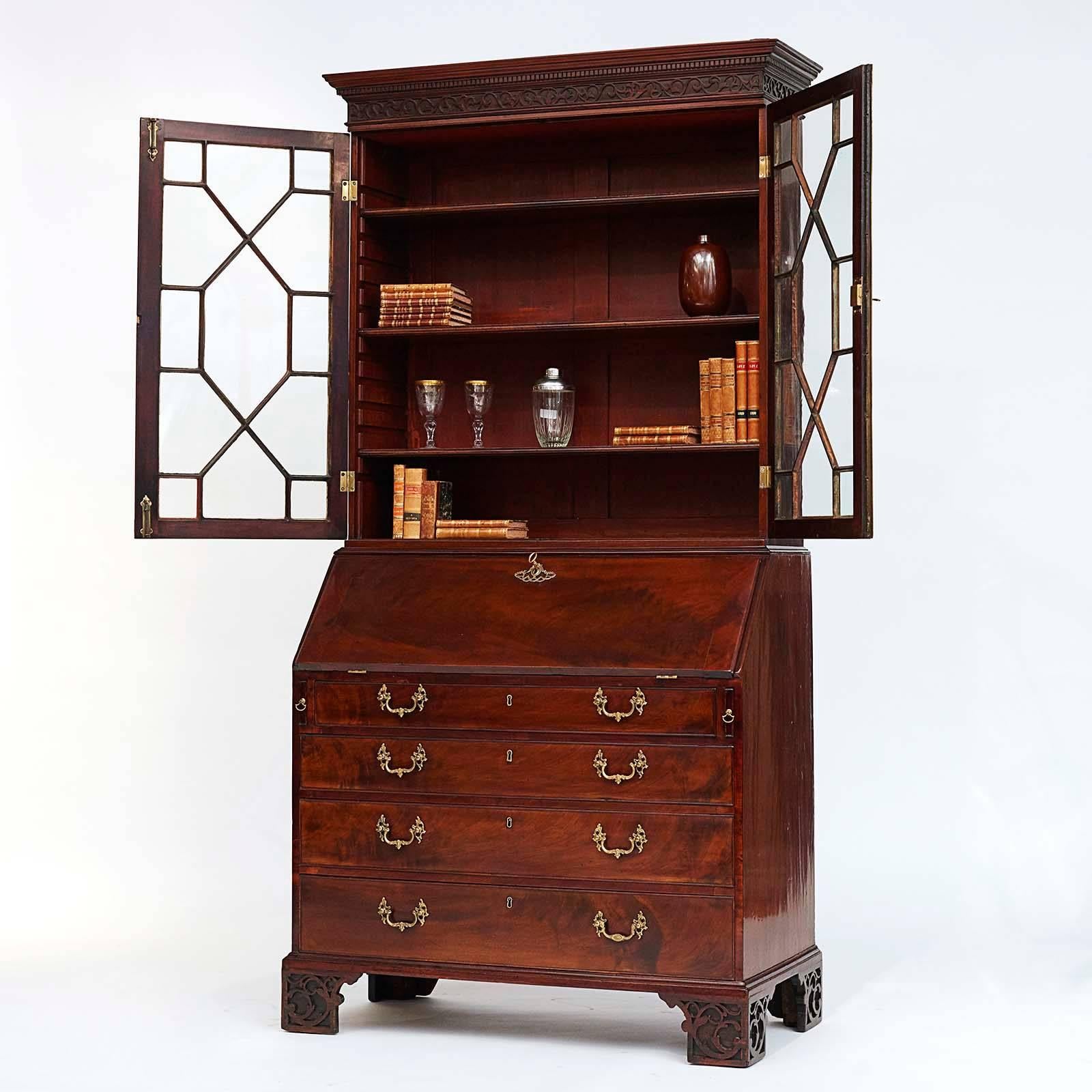 An English George III mahogany bureau bookcase, circa 1770s, the overhanging cornice with a carved leaf scrolled frieze, above a pair of astragal glazed doors, the slant front opening to a fitted interior with drawers and pigeon holes, above four