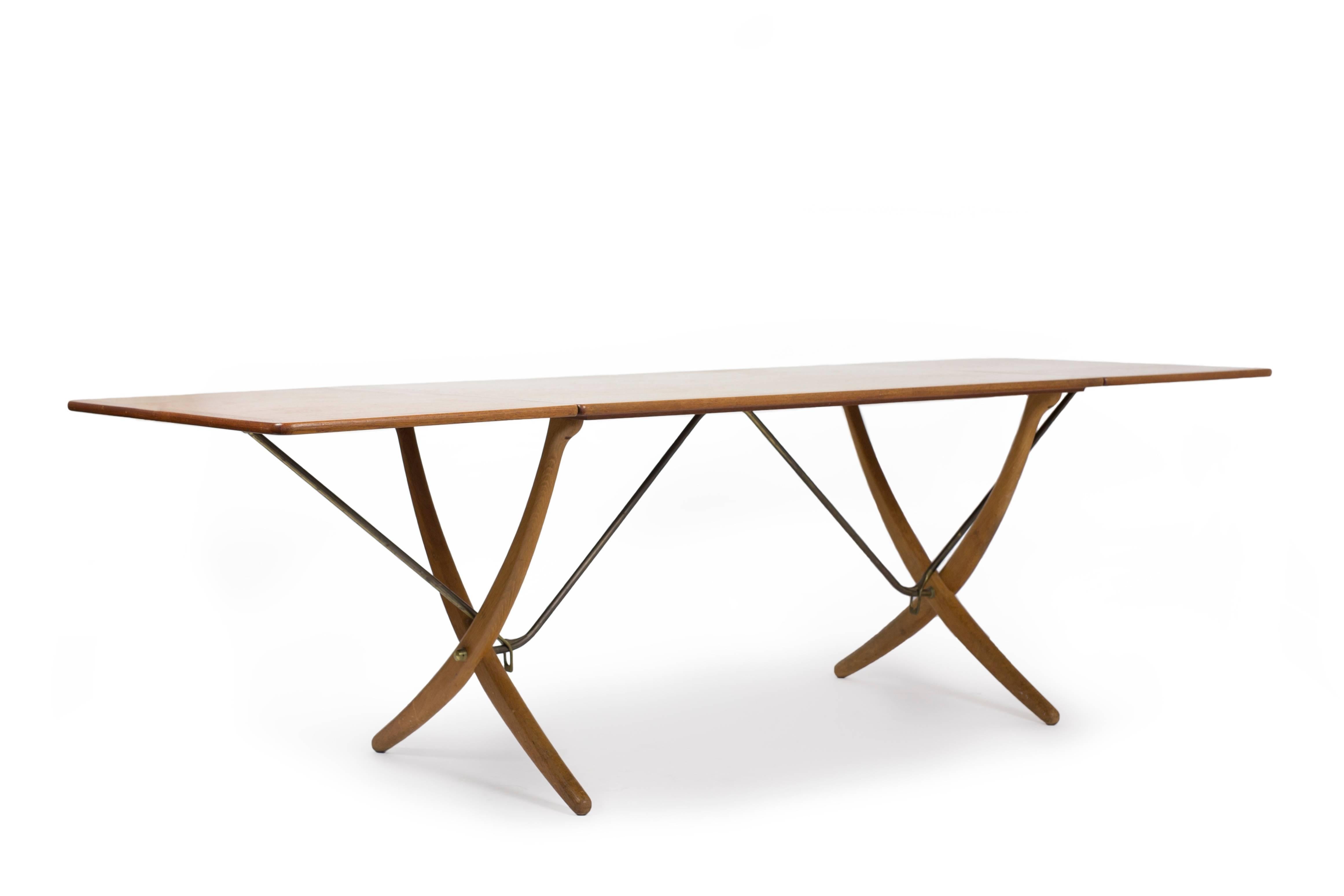 Hans J. Wegner teak dining table with two drop-leaves, cross-legs of patinated oak and stretchers of brass. 
Designed by Wegner 1950 and manufactured by cabinetmaker Andreas Tuck, Denmark, model AT304. 
Measuring 128 cm /50 Inches or 238 cm / 94