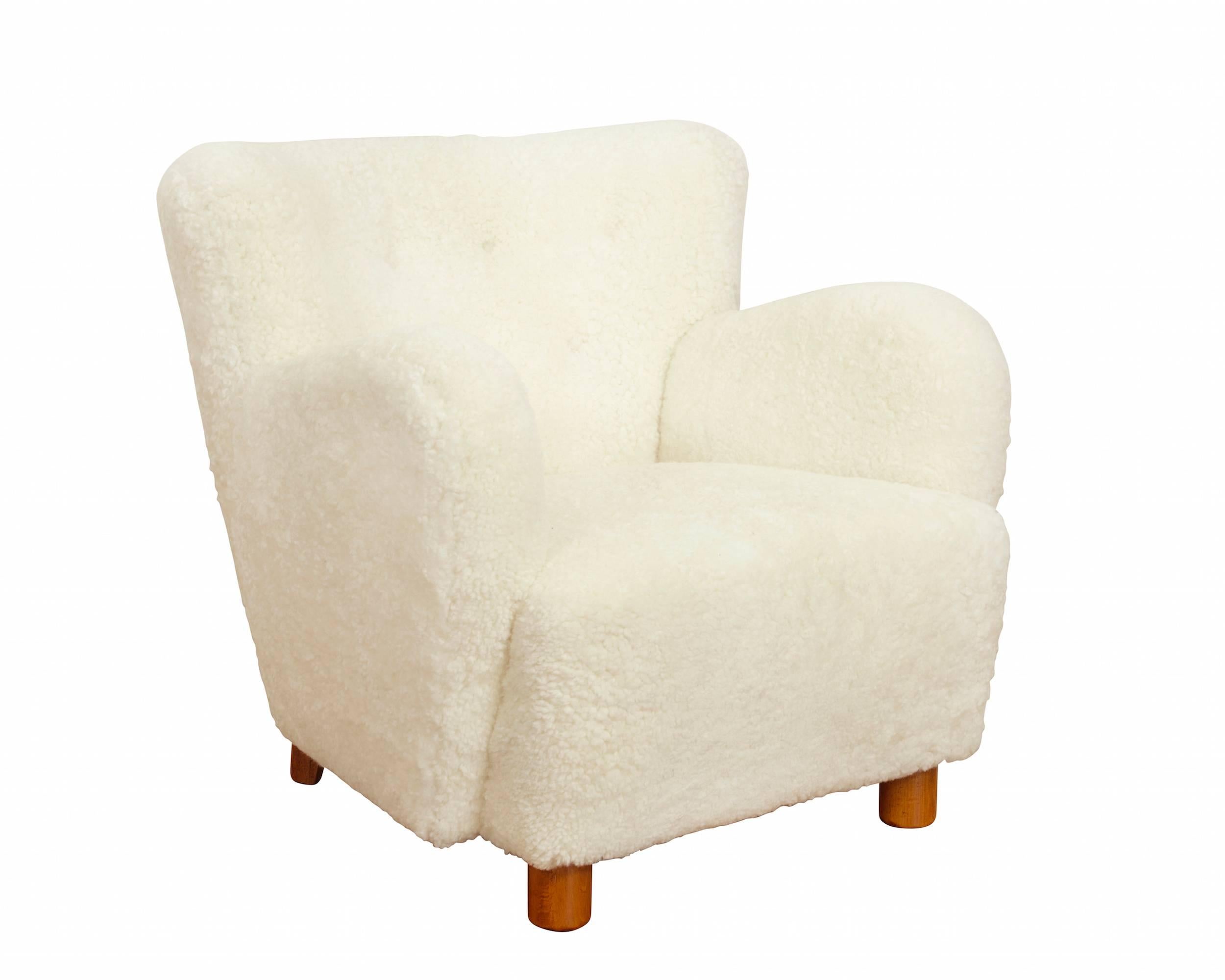A pair of lounge chairs upholstered in ivory sheepskin, raised on legs of browned beech.