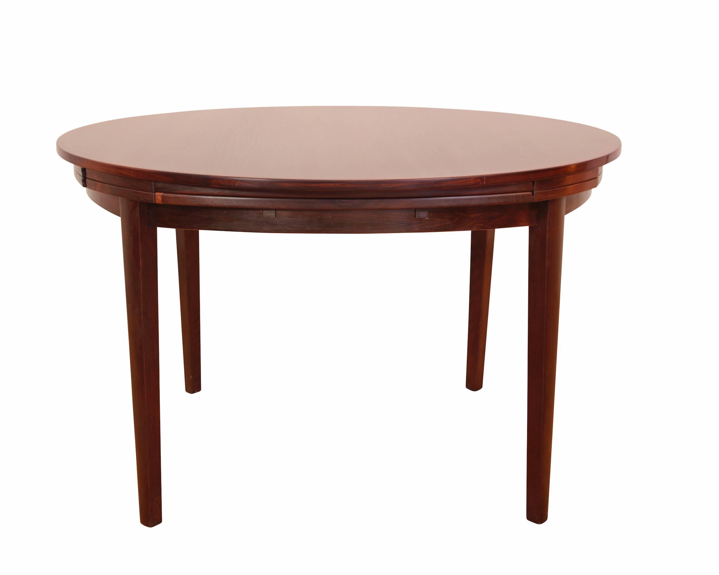 Round rosewood dining room table with pull-out leaves, raised on for legs.
Designed and manufactured by Svend Dyrlund. 

Measurements taken when closed.