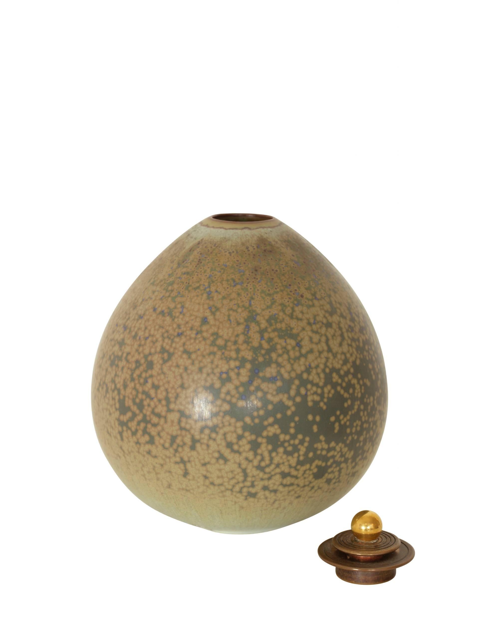 Stoneware vase with green and grey spotted glaze and partly gilded bronze lid.
Artist and manufacturers signature, numbered 21030.