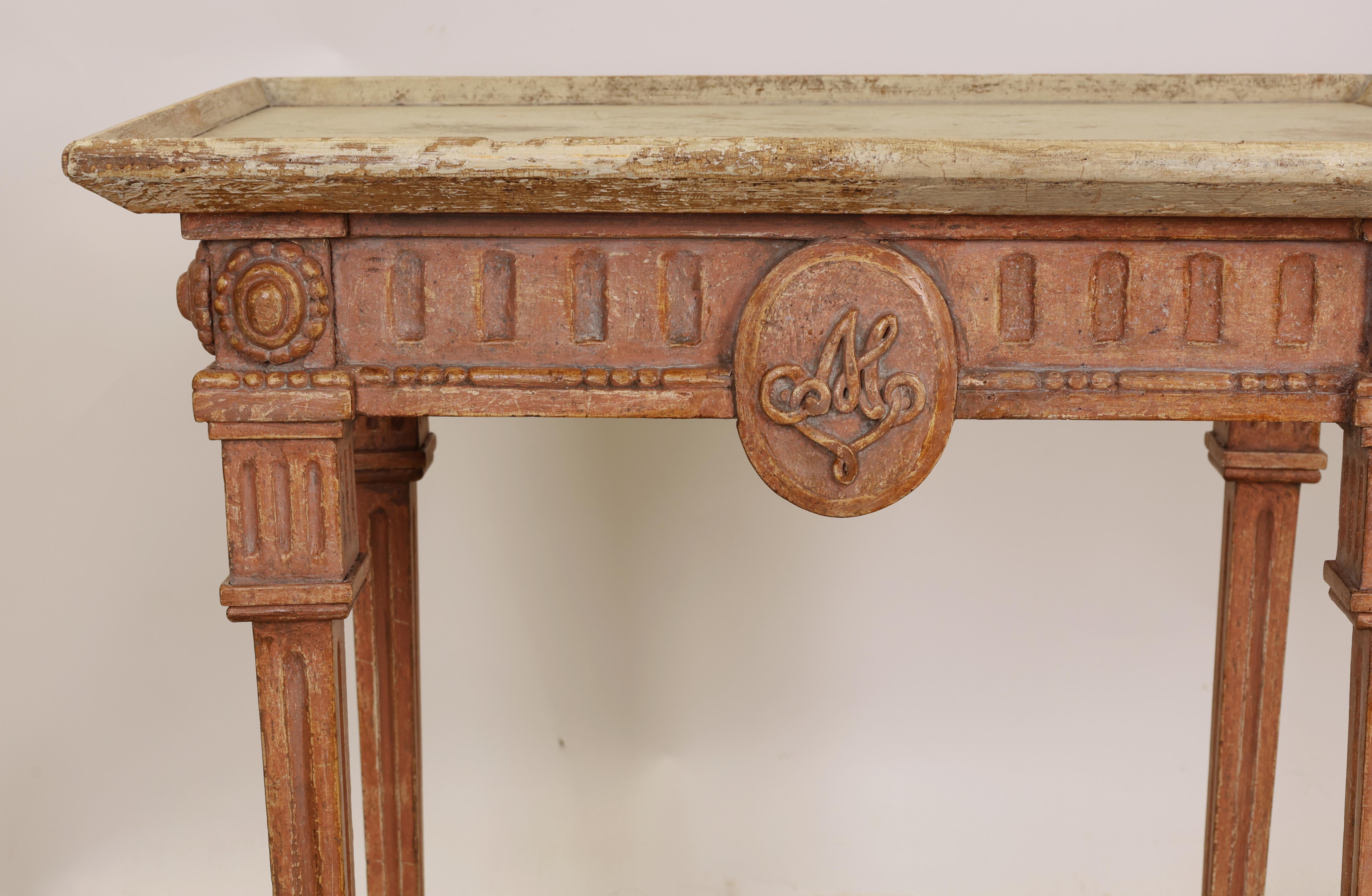 A Gustavian tray table from southern Sweden with a carved wooden monogram on both sides of the apron. The table is freestanding. It features carved decorative details, such as fluting and beading.