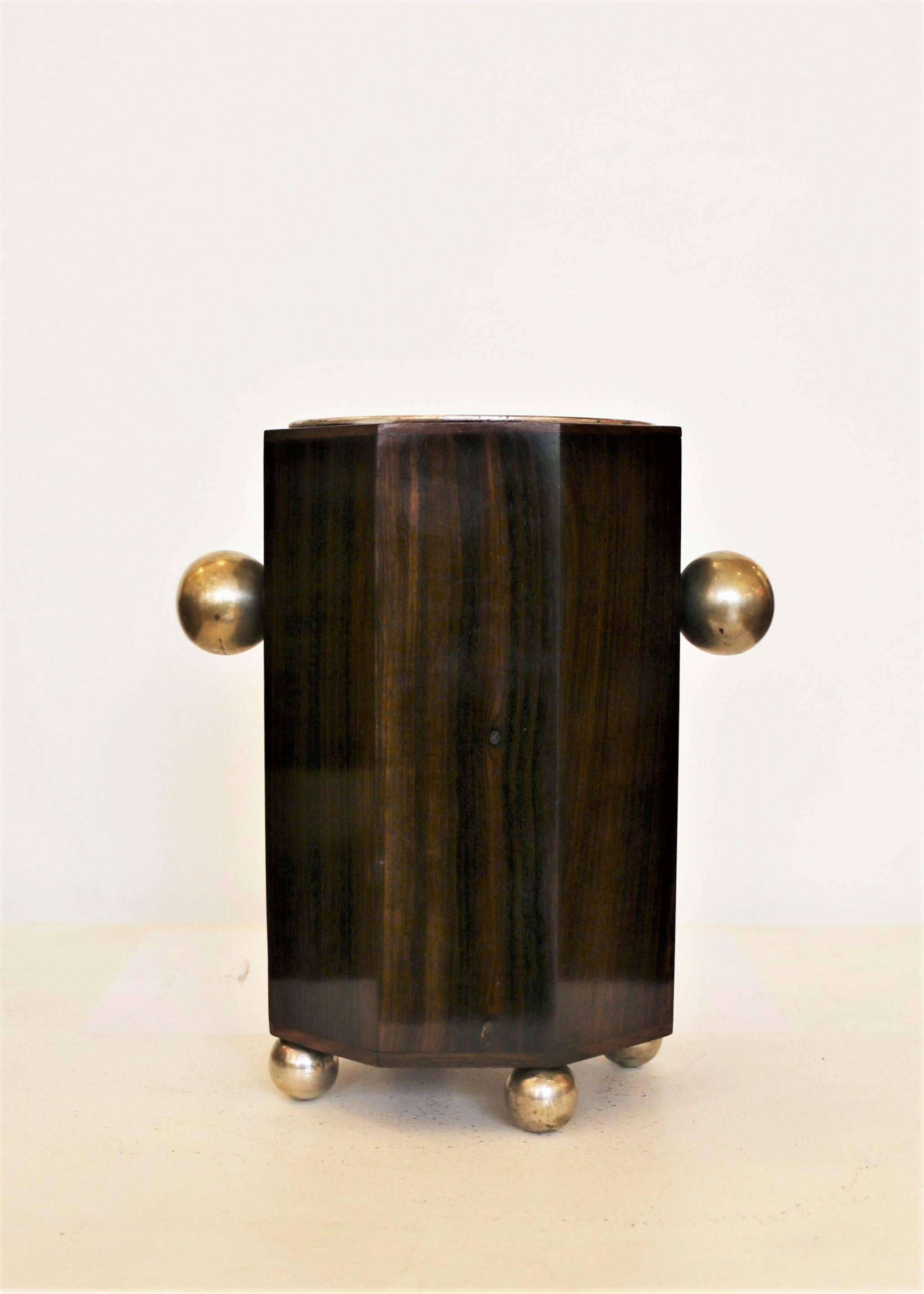 Art Deco wine cooler. Nickel-plated metal inside and Macassar ebony veneer. There are two nickeled handles on the sides, and four spheres serving as legs for the cooler.
It can be used as wine cooler (its original use) or as a flower