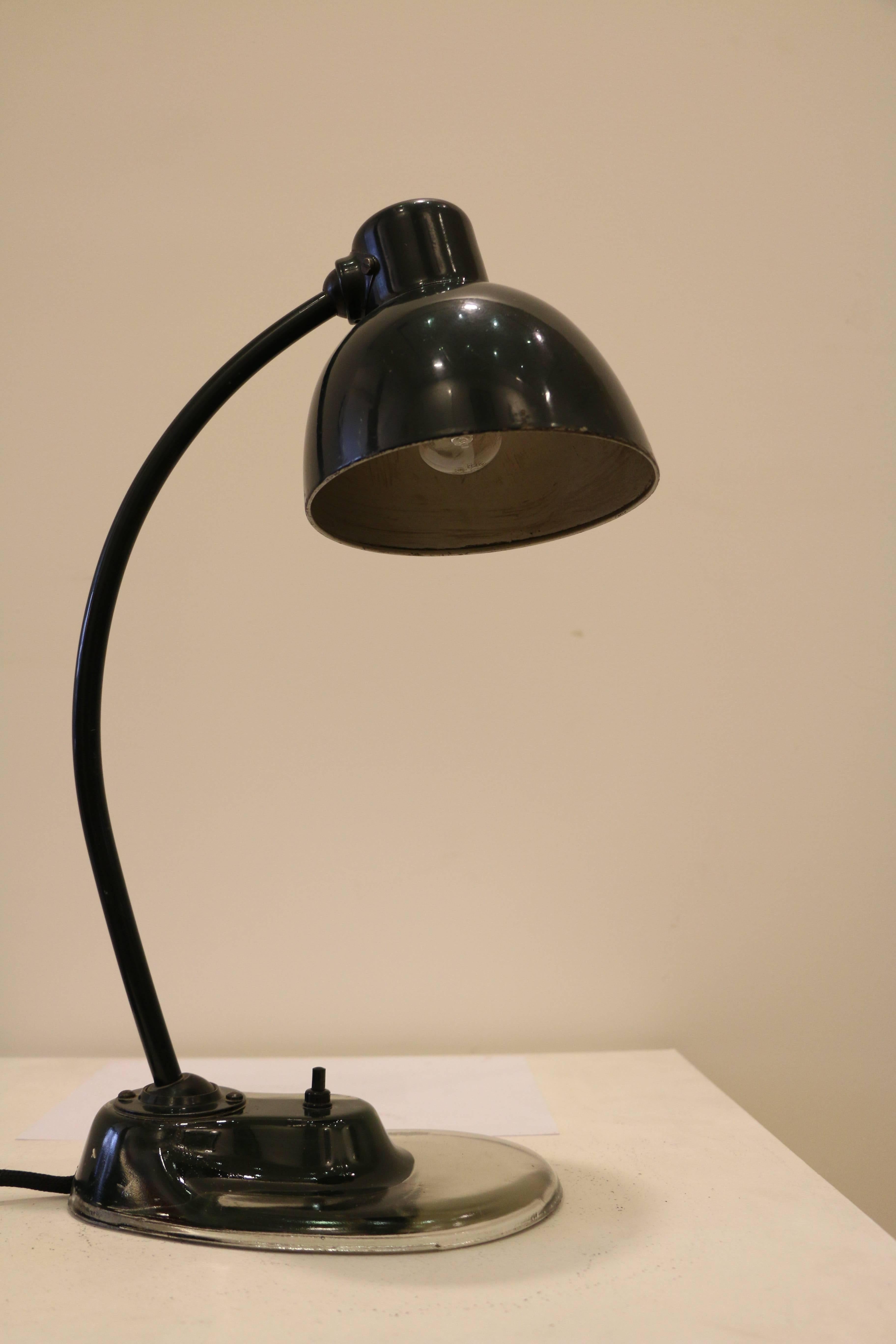 Emblematic Bauhaus desk lamp designed by Marianne Brandt (1893 - 1983) and manufactured by Kandem. It has the typical glass base which makes this model the much sought after one. Original dark green paint. 
Fully functional.
Wired for European