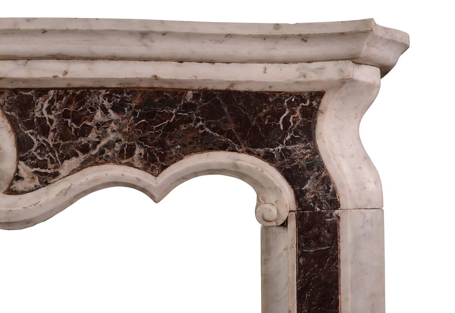 A petite Italian Carrara and Rosso Levanto marble fireplace. The moulded jambs surmounted by shaped frieze featuring carved classical Anthemion leaf to centre. Moulded shelf above. Unusually small, well suited for a bedroom or study. From Northern