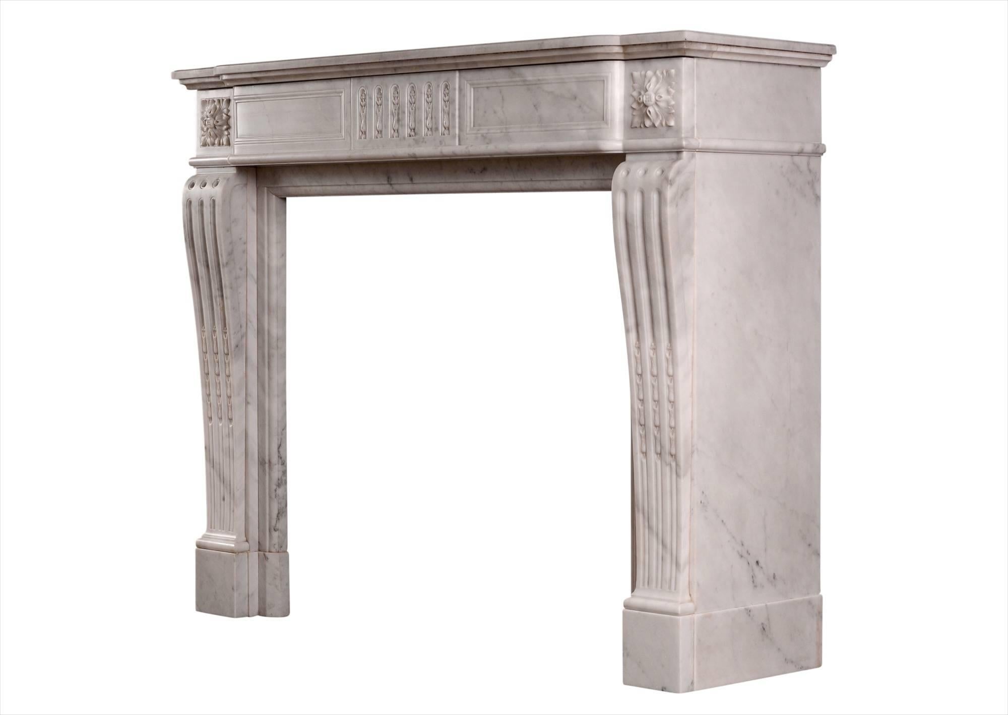 A 19th century French Carrara marble fireplace in the Louis XVI style. The shaped, fluted jambs with carved inlaid husks, surmounted by carved square paterae. The panelled frieze with matching inlaid flutes. Bowfronted moulded shelf.

Measures: