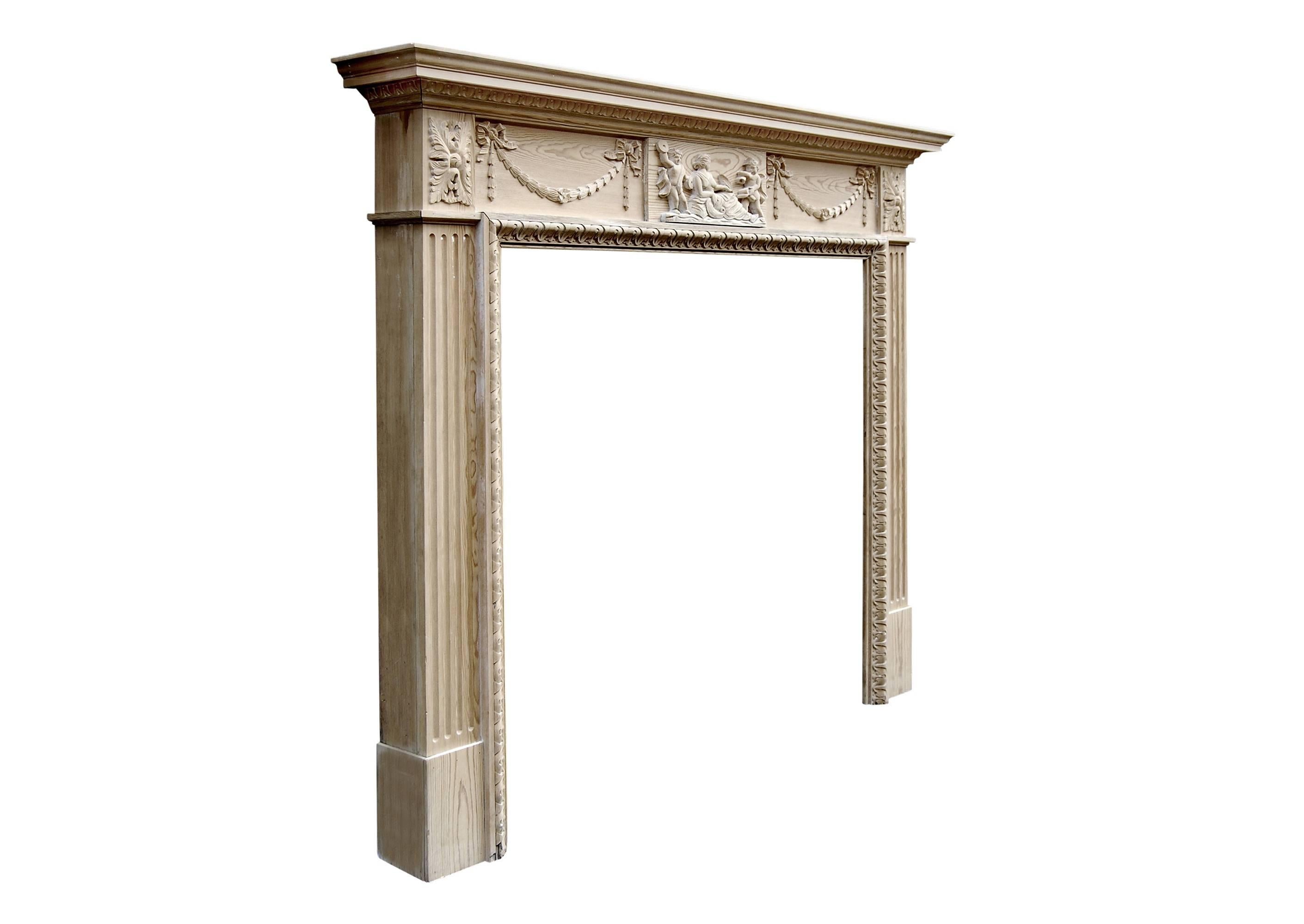 20th century English stripped pine fireplace. The centre carved with female and putti, the frieze with tied ribbon bellflower swags, fluted jambs surmounted by carved leaf paterae. Egg and dart cornice and leaf inner leg moulding.

Measures: Shelf