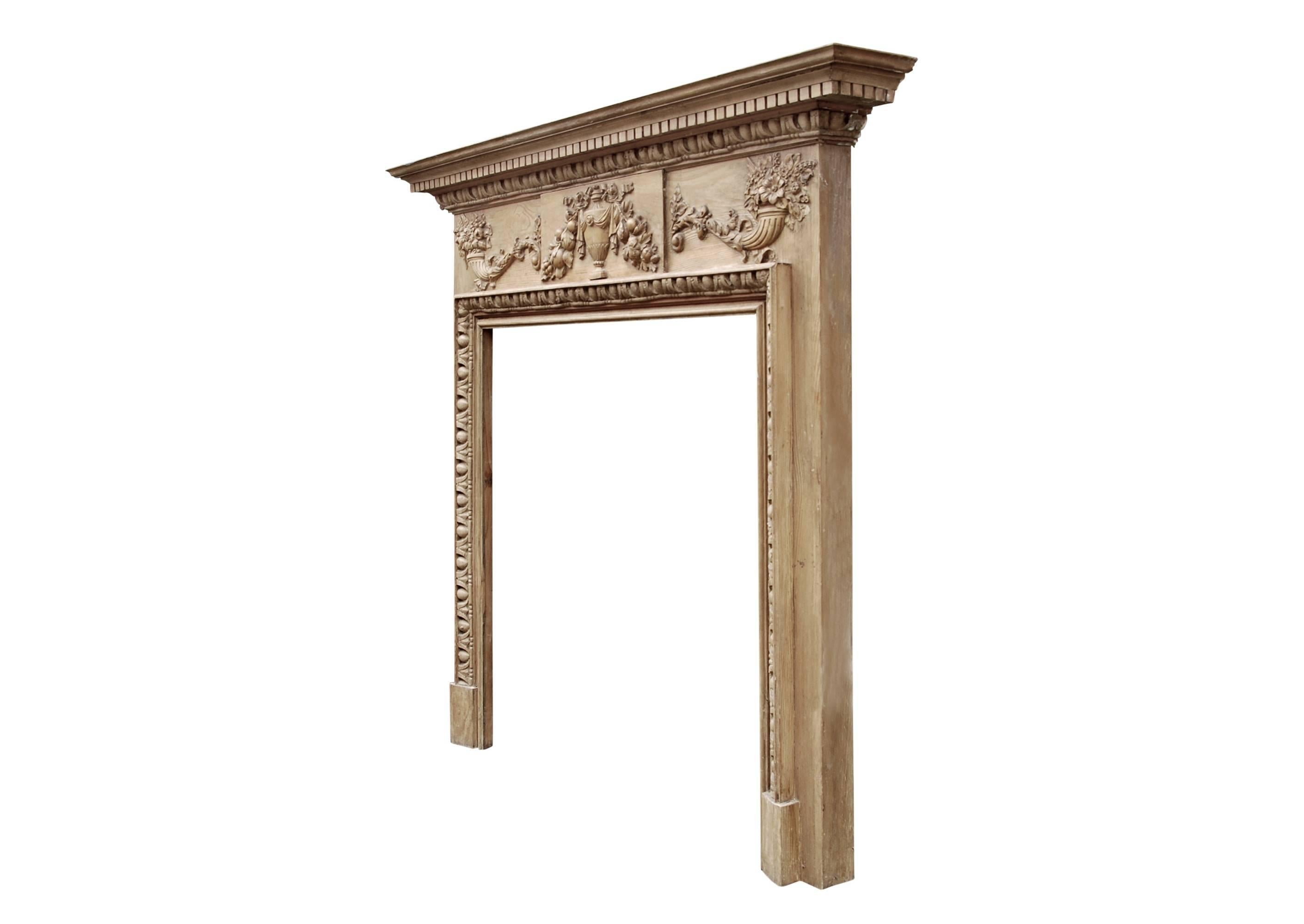 An English Georgian style pine fireplace with gesso enrichments. The frieze with centre blocking of urn tied with ribbon, juxtaposed with Cornucopia holdings leaves and fruit with ornate foliage. Egg-and-tongue carved mouldings to jamb in grounds