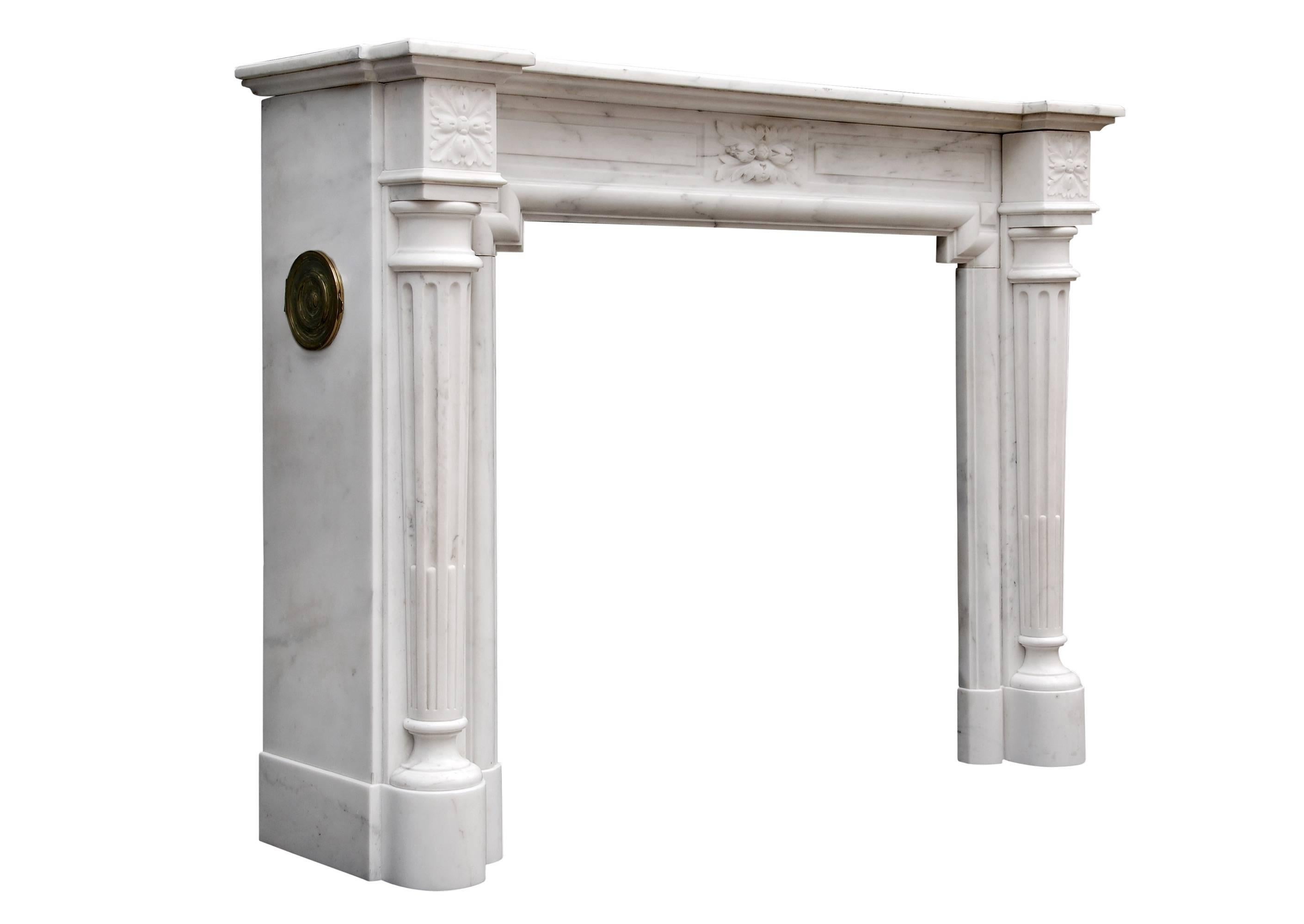 An elegant 19th century French Louis XVI fireplace in Statuary marble. The tapering stop-fluted columns surmounted by carved end blockings, the panelled frieze with carved leaves to centre, the returns with brass vents. Breakfront