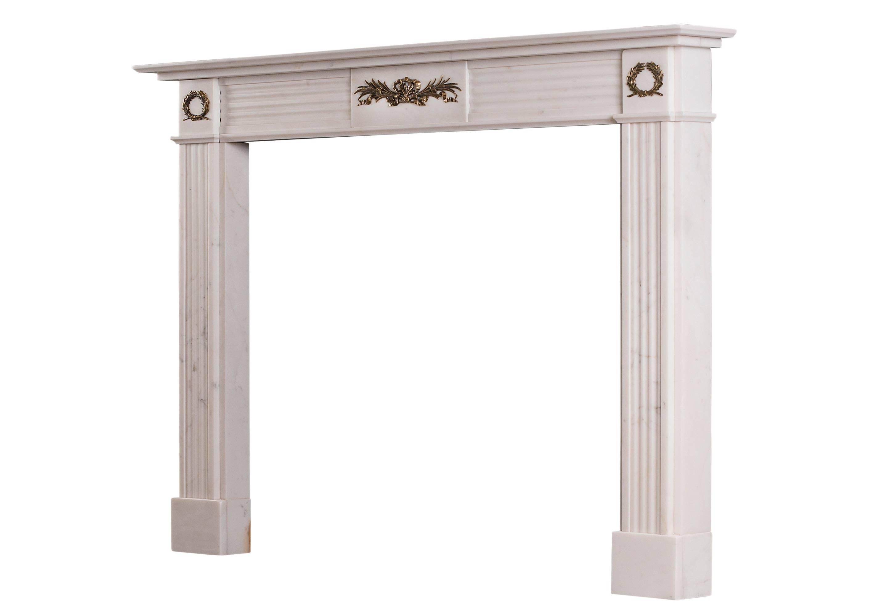 A statuary white marble fireplace in the Regency style. The reeded jambs surmounted by brass ormolu wreaths. The reeded frieze with centre plaque featuring ormolu adornment of tied foliage and cascading ribbons. English, 20th century.

Shelf