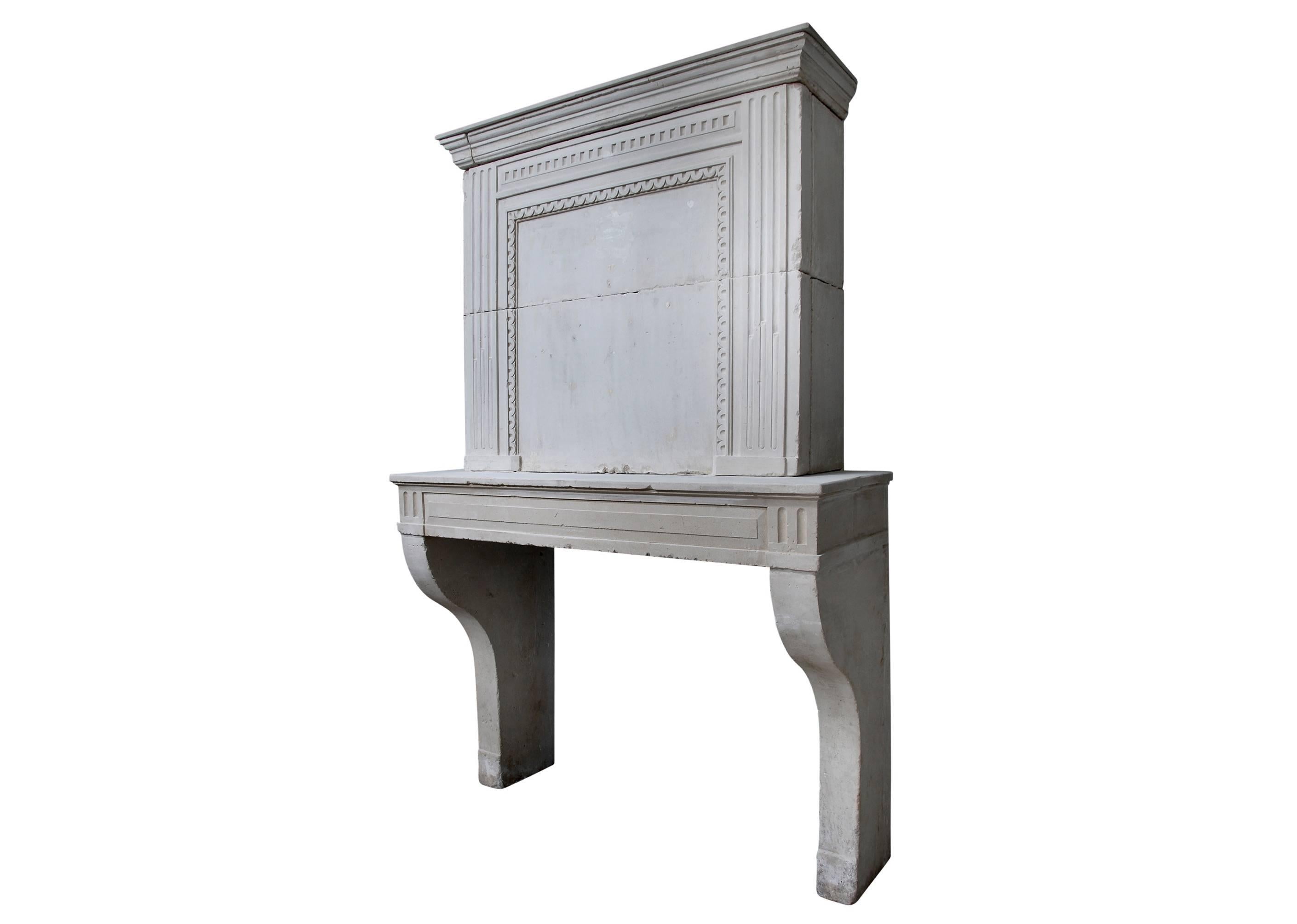 A late 18th century French Louis XVI limestone fireplace, with shaped jambs, panelled frieze with fluted blockings. The trumeau with panelled centre and dentil and fluted decoration beneath moulded cornice. A rustic piece in good condition. PRICED