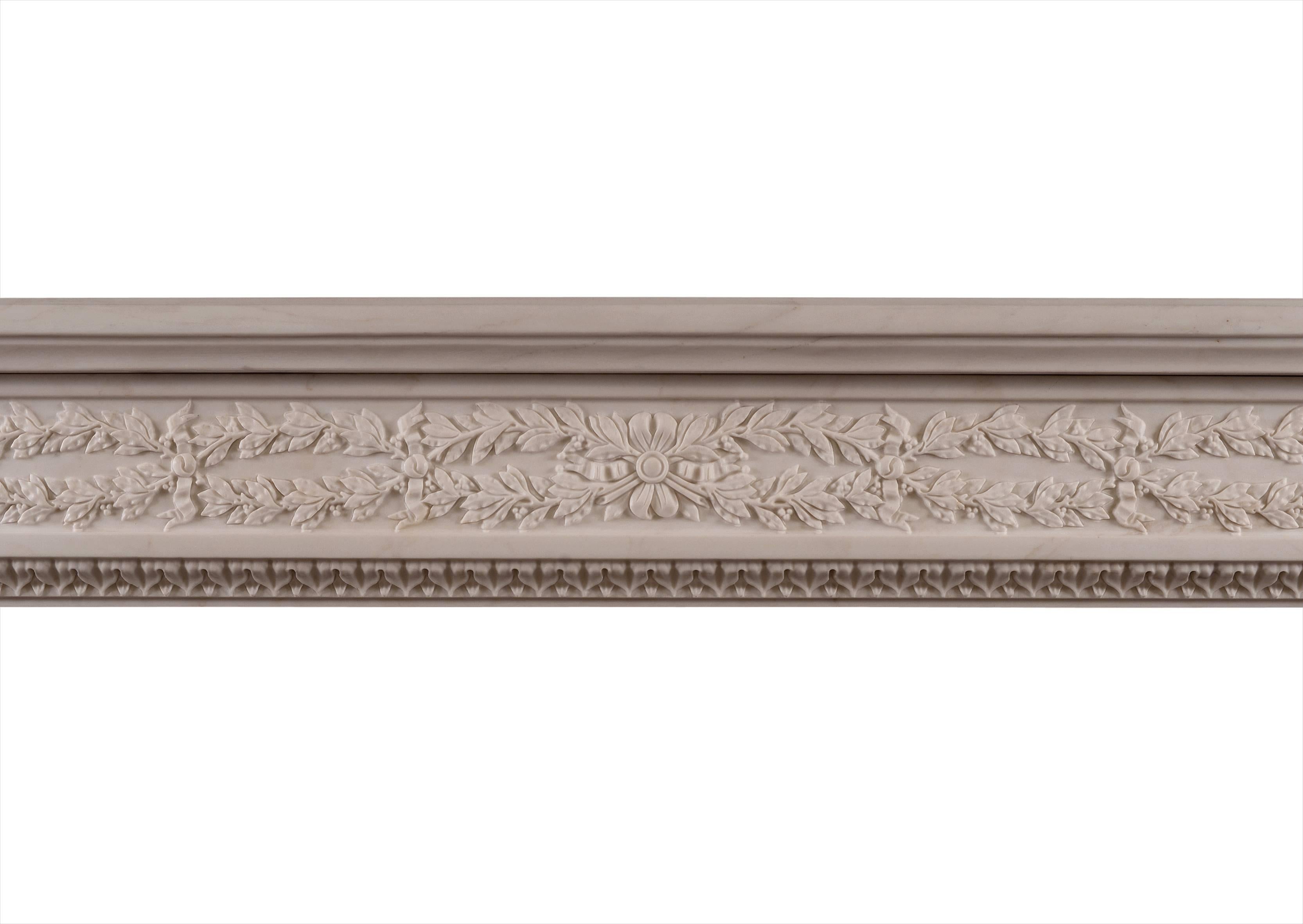 A French Louis XVI style white marble fireplace, with carved frieze of interlocking leaves, berries and ribbons. The jambs with tapered half round columns with flutes and husks surmounted by capitals of stiff leaf form. The inner moulding with