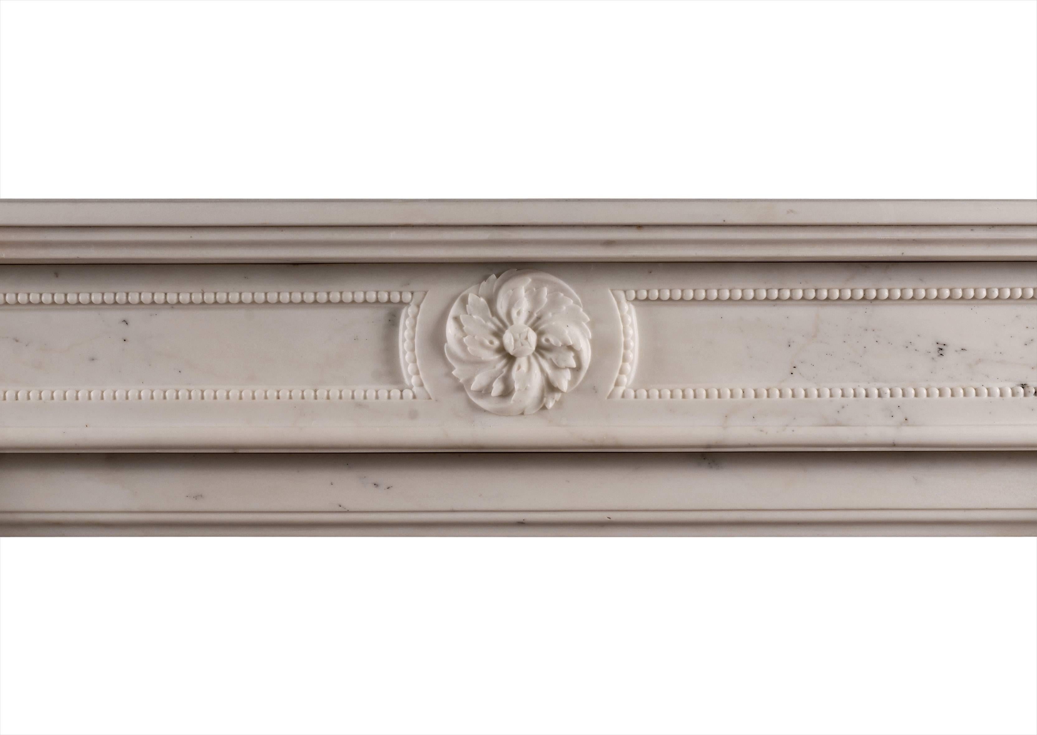 An elegant Statuary white marble fireplace in the Louis XVI style. The shaped jambs with carved rope moulding t0 centre, surmounted by carved swirling paterae to end blocks. The panelled frieze with matching patera and fine beading. Moulded shelf,