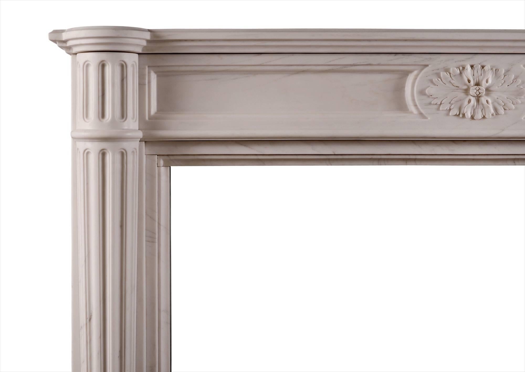 Ein französischer Kamin aus weißem Marmor im Louis-XVI-Stil. Der getäfelte Fries mit ovaler Mittelpatera. Halbrunde, spitz zulaufende Säulen, die von passenden kannelierten Blöcken gekrönt werden, darüber ein profiliertes Regal. Eine Kopie eines