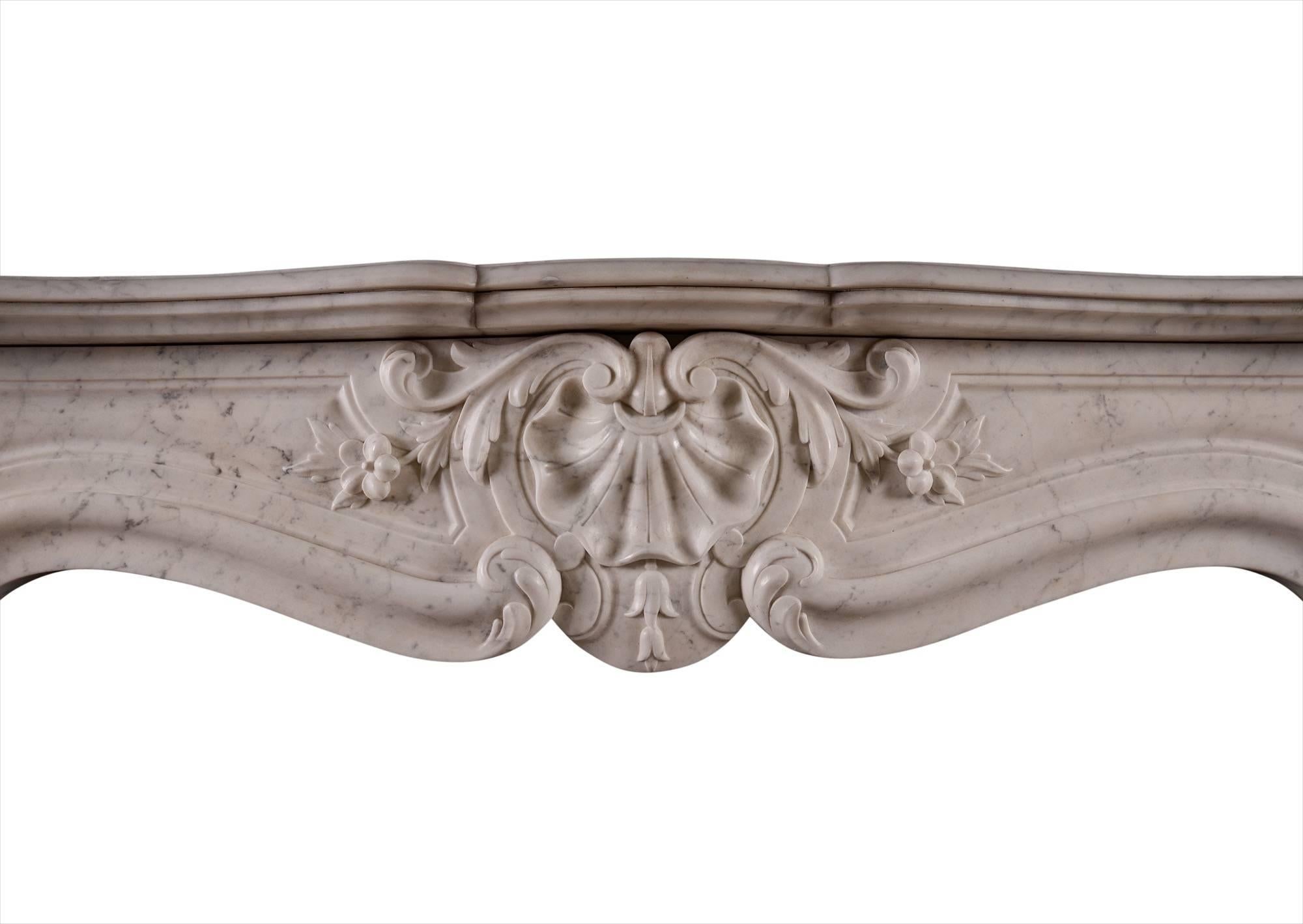 A 19th century French Louis XV style fireplace in Carrara marble. The jambs with stiff acanthus leaves to base, surmounted by carved shell and scroll work. The panelled frieze with carved shell to centre, flanked by foliage. Shaped, moulded shelf.