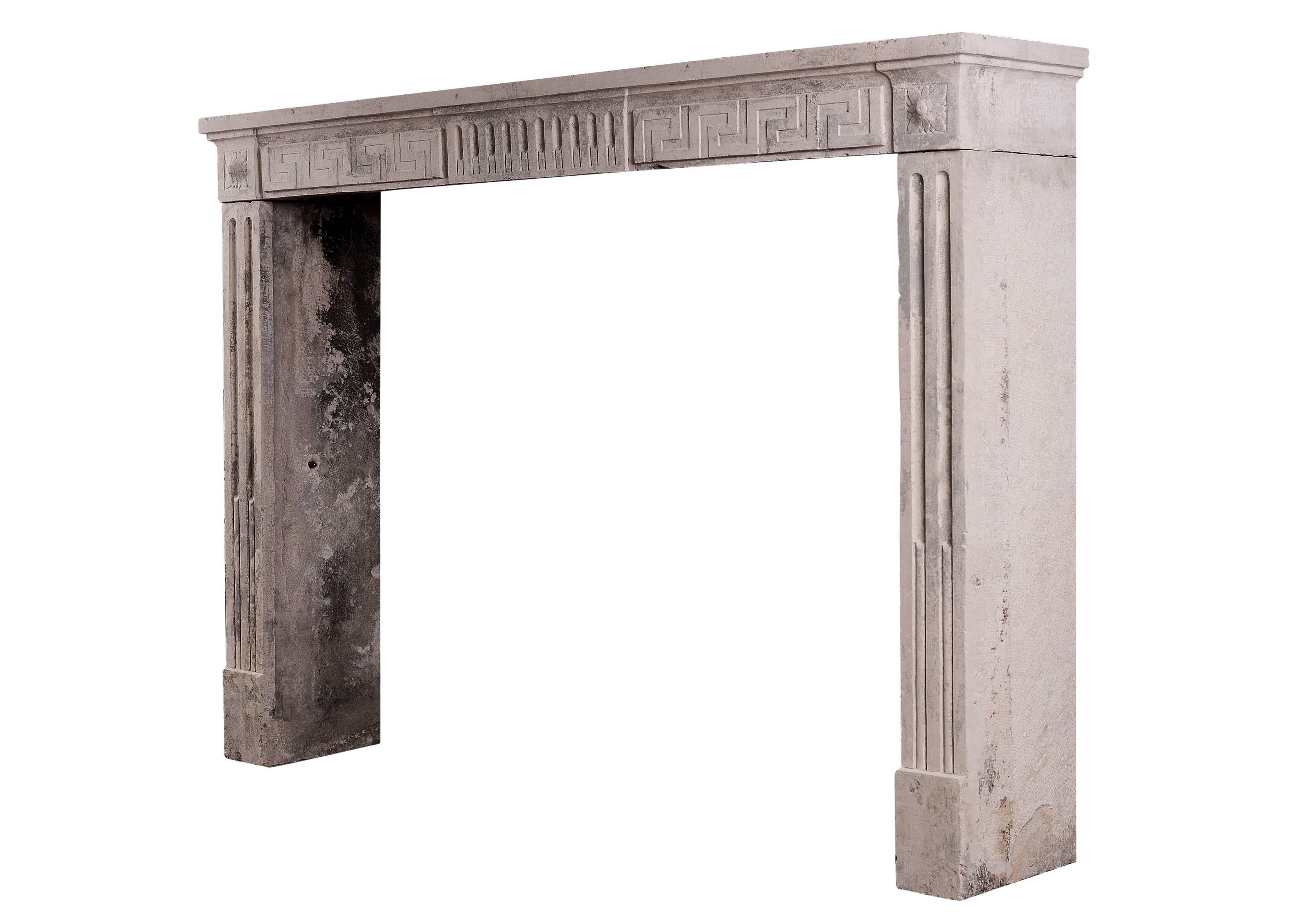 A rustic French period Louis XVI limestone fireplace. The frieze with stop fluting to centre panel and Greek key pattern. The fluted jambs surmounted by square carved paterae. Period 18th century. Some wear and patination consistent with