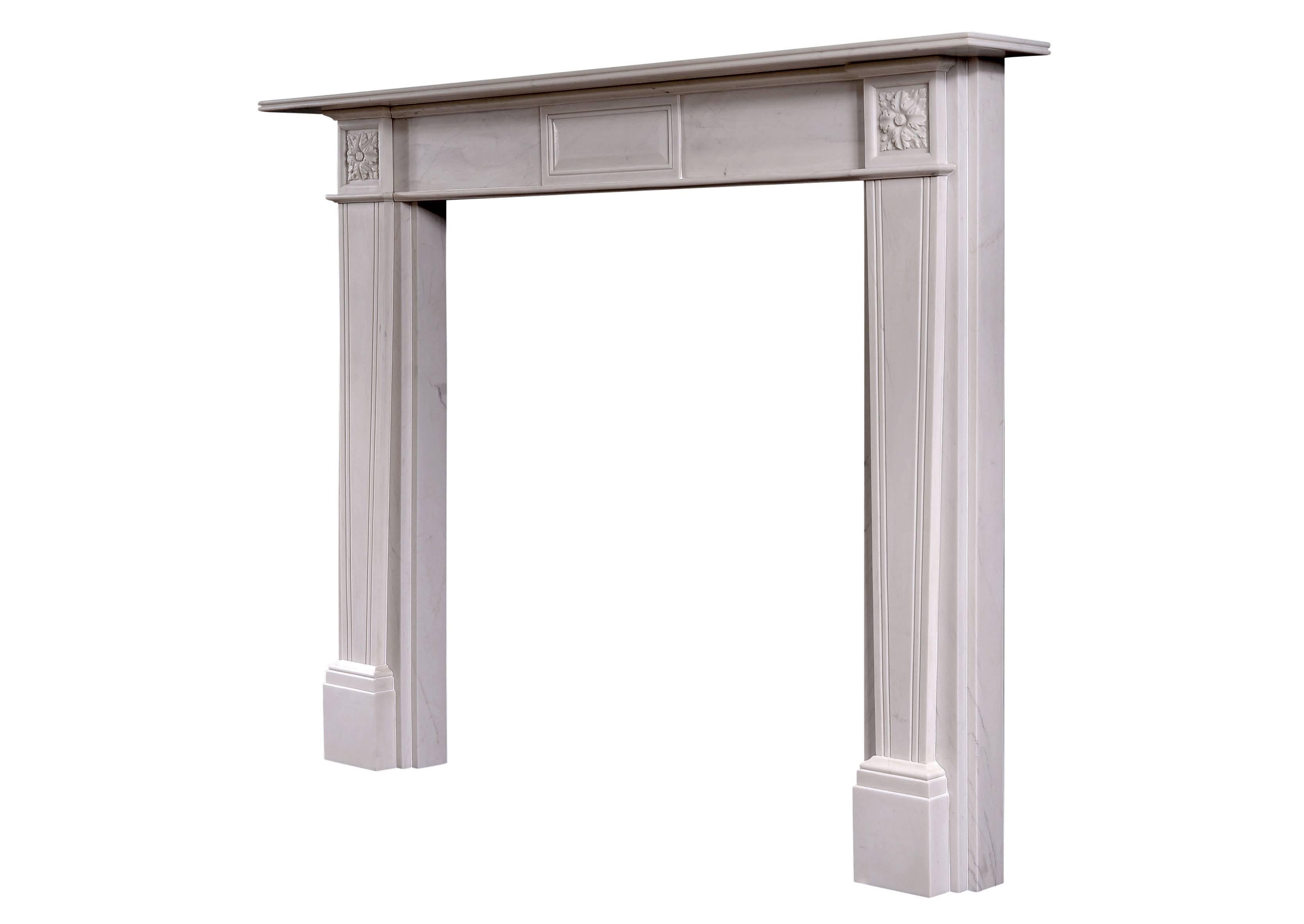 An English white marble fireplace in the early 19th century Regency style. The frieze with raised and fielded centre panel, the tapering reeded jambs surmounted by carved square paterae. Reeded shelf.

Measures: 
Shelf width: 1510 mm / 59 1/2