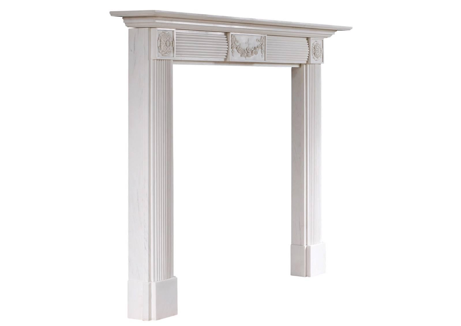 An English white marble fireplace in the Regency style. The jambs and frieze with matching bowed flutes and carved rosette paterae, the frieze with carved centre panel with swags and flowers. Stepped, moulded shelf. A good quality copy of a period