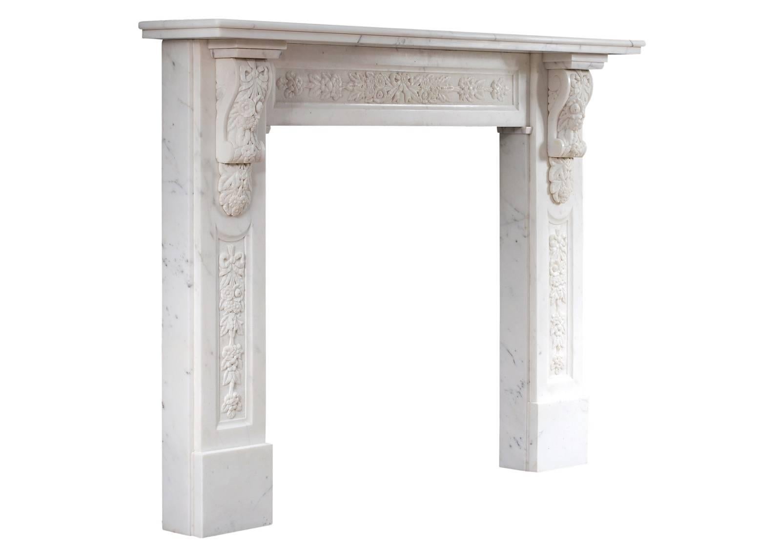 An early Victorian English statuary marble fireplace. The panelled jambs with carved flowers and foliage throughout surmounted by tied ribbons. Elaborately carved corbels above featuring cascading foliage and leafwork. The panelled frieze with