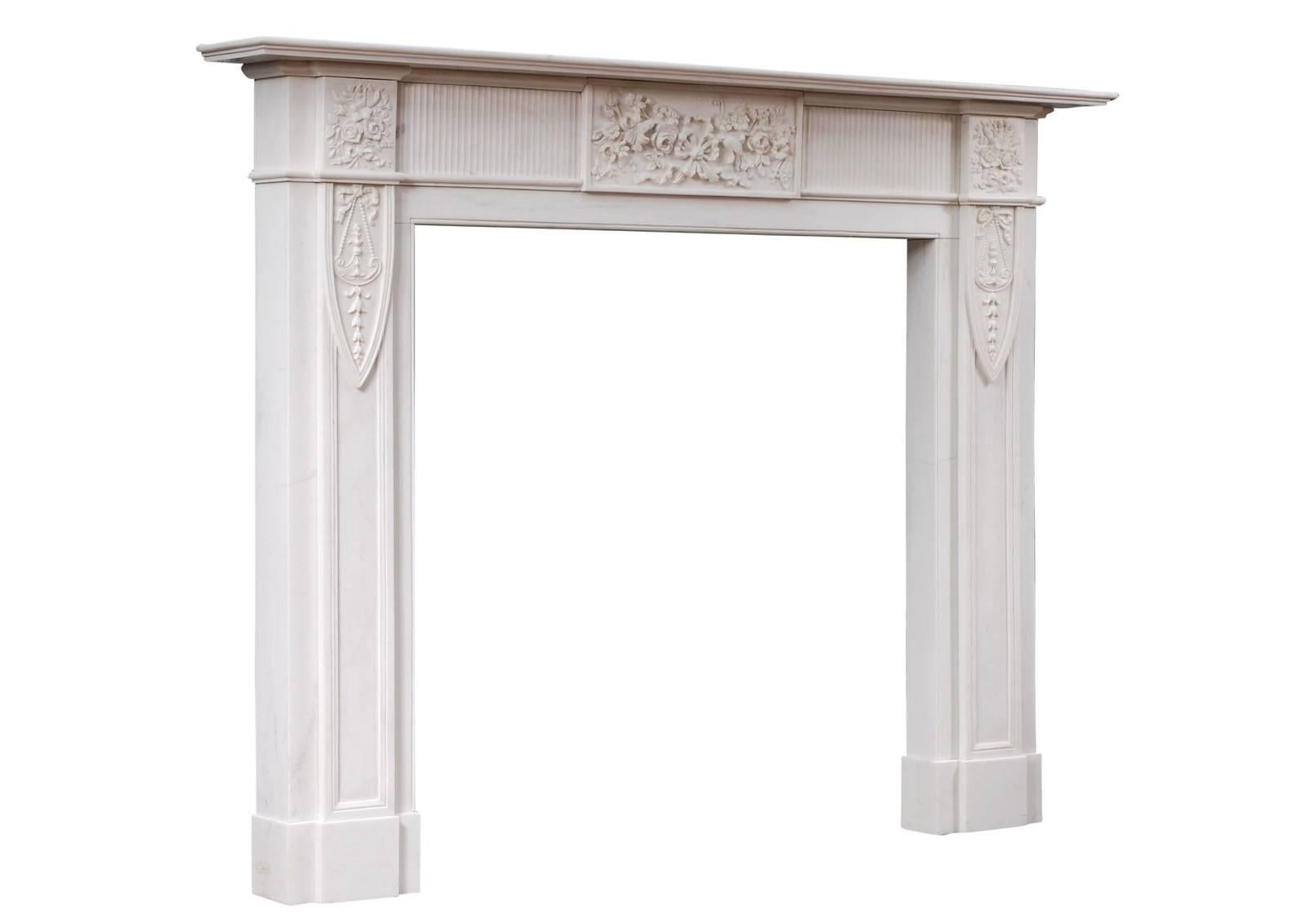 Une cheminée anglaise en marbre blanc pur. La frise sculptée avec un bloc central et des blocs d'extrémité présentant des fleurs et des feuillages attachés par des rubans. Les jambages à panneaux sont sculptés de rubans et de boucles d'oreille.