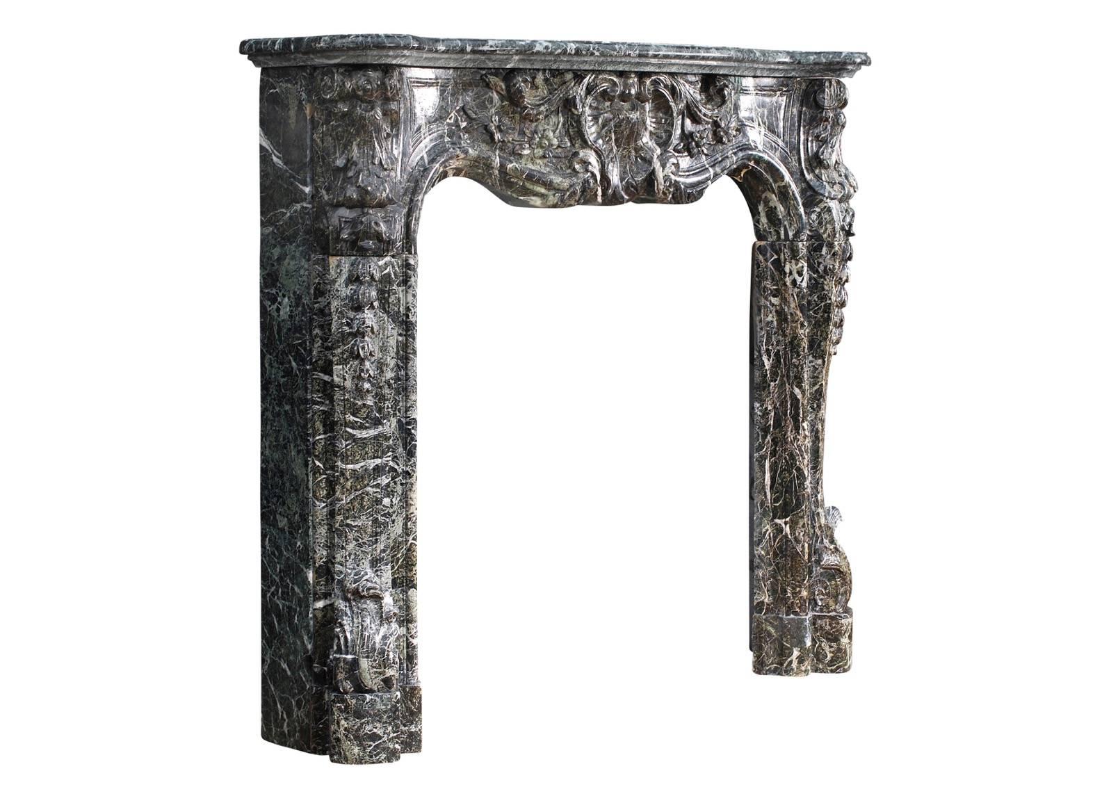 A 19th century French Louis XV style fireplace in Tinos green marble. The heavily carved panelled frieze with shells, flowers and foliage. The jambs with carved shells surmounted by belldrop flowers and stiff acanthus leaves to base. Shaped moulded