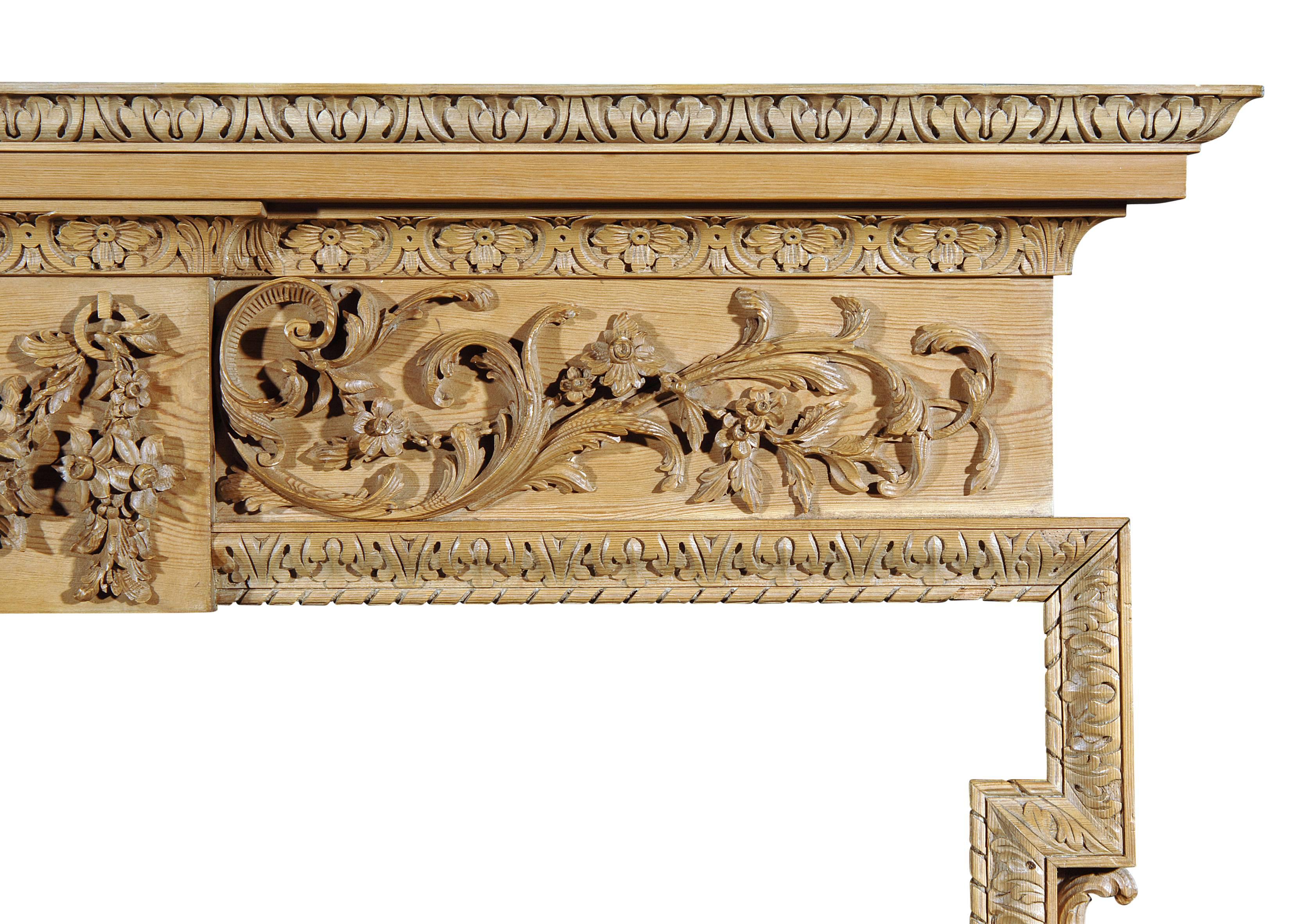 An English George III style pine fireplace, with carved festoon centre of leaves, fruit and flowers, scrolled and leaf side panels, acanthus leaf cornice and leg moulding. Carved scroll and leaf brackets to jambs. Width across plinths is 72.75?.