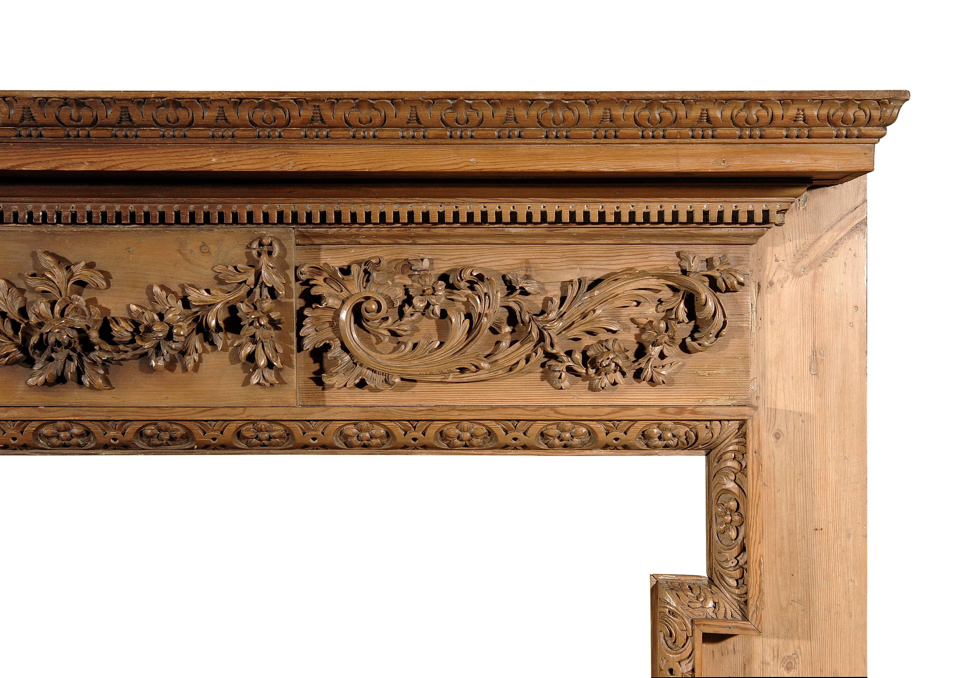 A 19th century George III style pine fireplace with carved festoon centre of fruit, flowers and leaves, side panels with scrolls and foliage, dentil and leaf cornice, and carved flower leg moulding.

Shelf Width:	1520 mm      	59 7/8 in
Overall