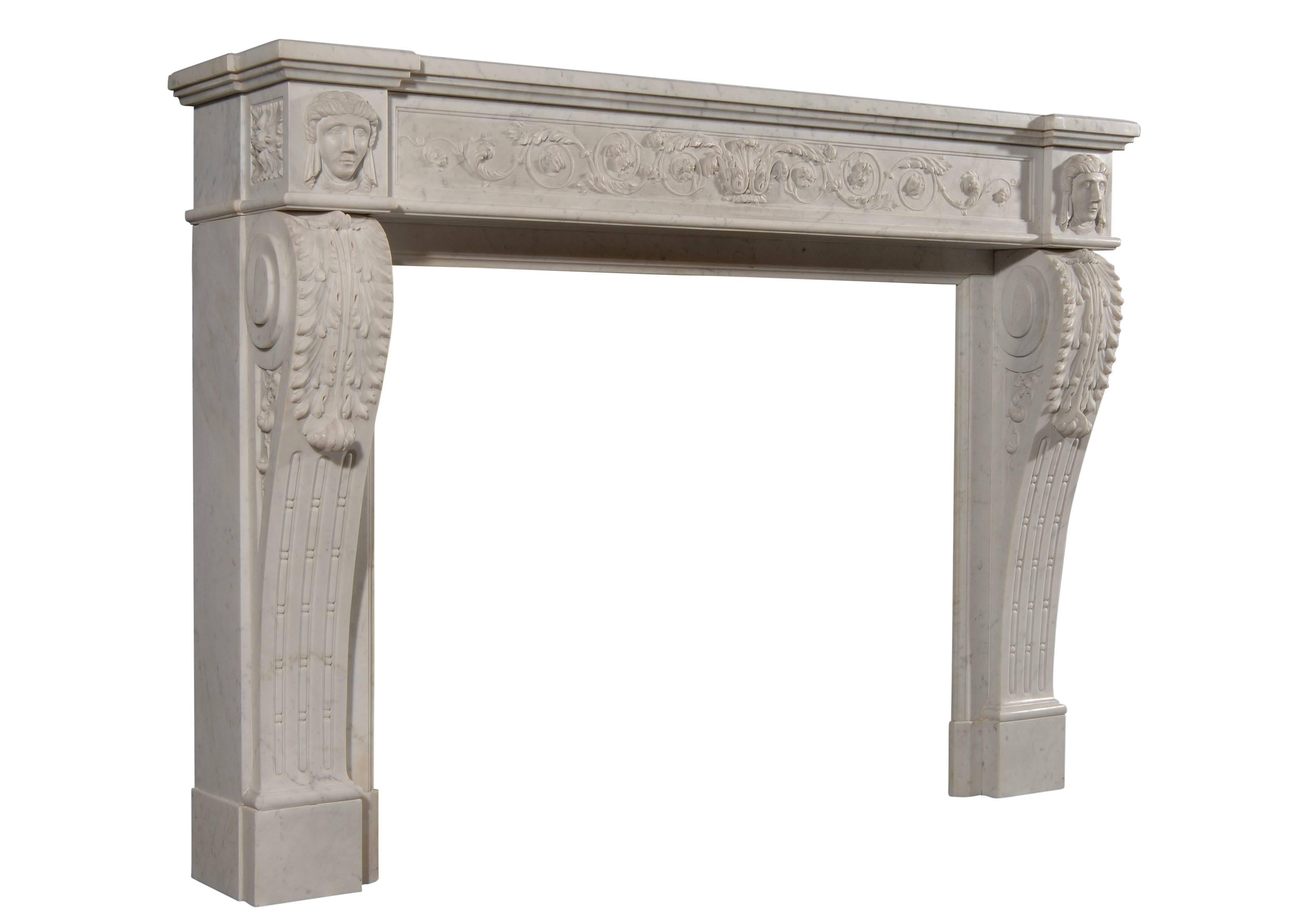 An unusual and nicely carved 19th century (circa 1840) French XVI style Carrara marble fireplace. The frieze with scrolled foliage. The shaped jambs with acanthus leaves, surmounted by side blockings with carved female faces and square paterae to