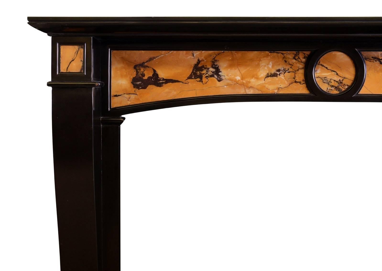 Une étonnante cheminée française de style Louis XVI en marbre noir belge et marbre italien de Sienne. Les montants massifs et façonnés sont surmontés d'une frise arquée avec des panneaux de Sienne incrustés. Étagère moulée à peu près. Deux marbres