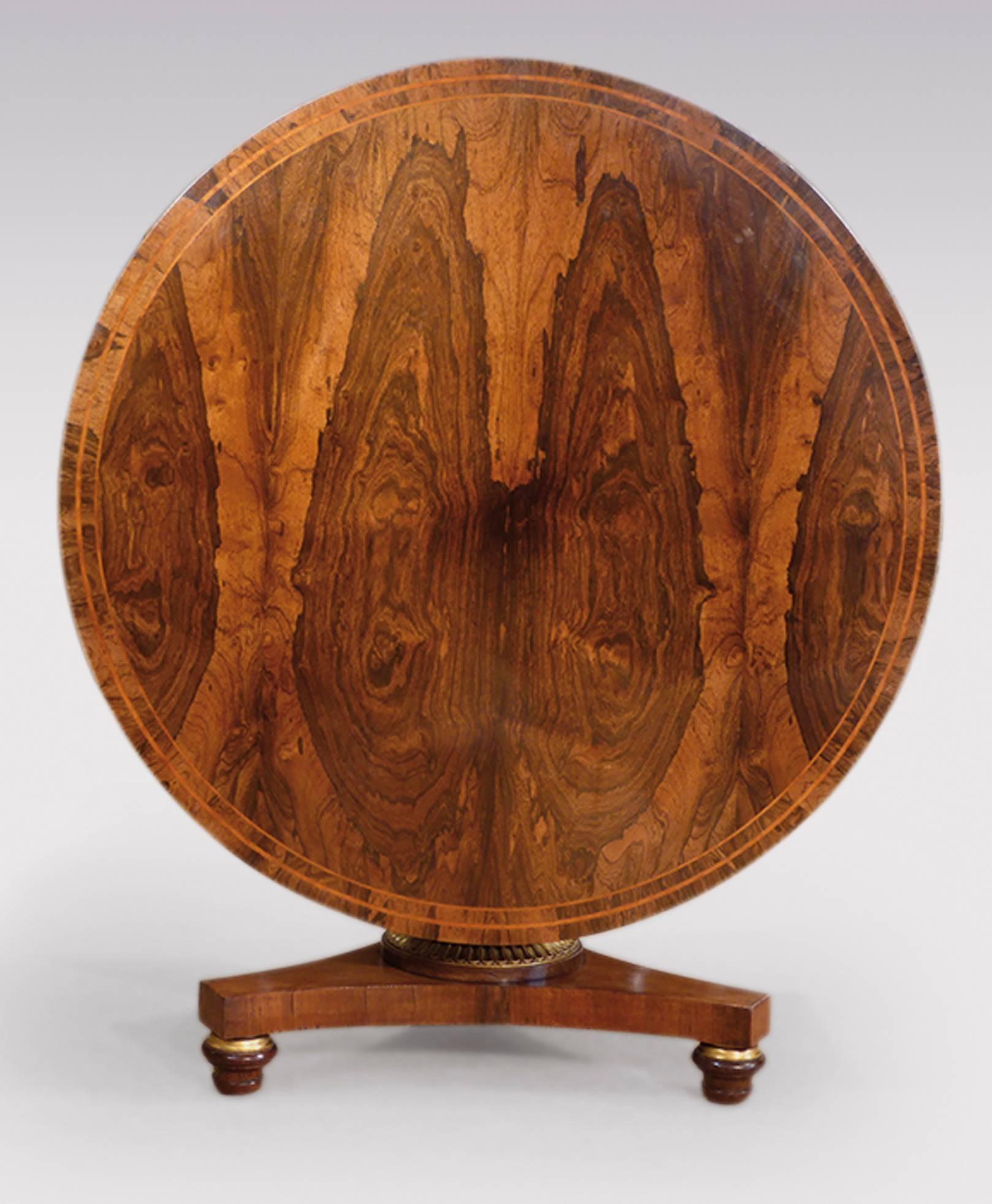 An early 19th century Regency period rosewood breakfast table, having satinwood line inlaid crossbanded circular top, with stunning book-matched veneers, raised on simulated and carved gilt turned stem, supported on concave triform platform base,