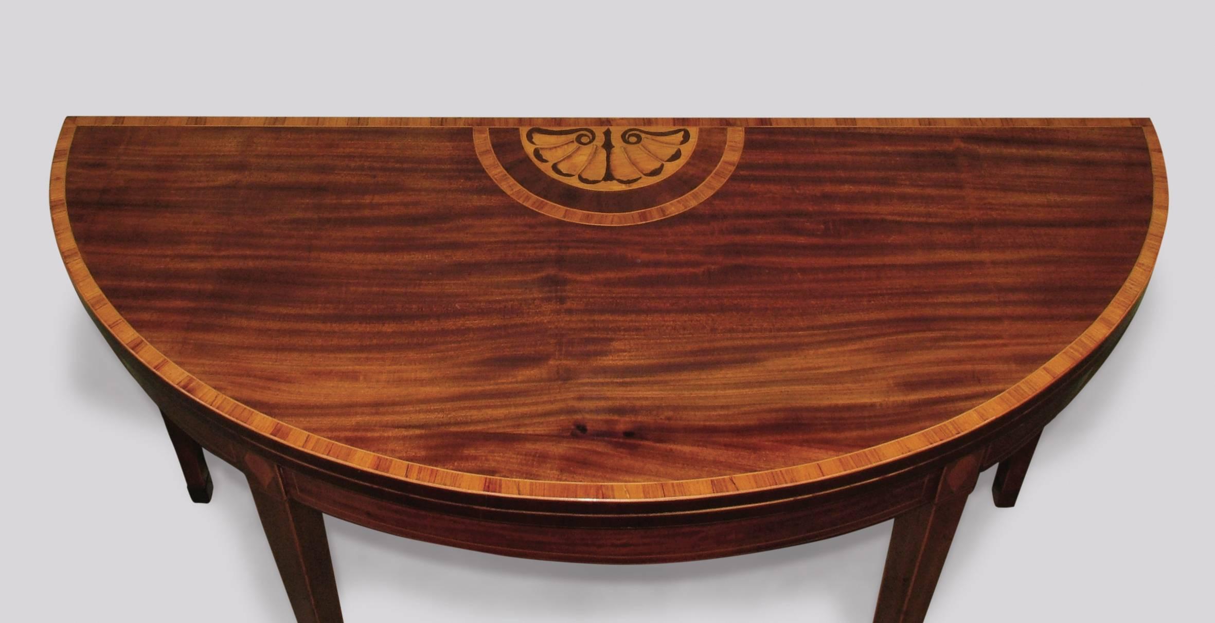 A late 18th century Sheraton period figured mahogany demilune card table of unusual large proportions, having tulipwood crossbanded top with central shell panel above boxwood and ebony strung frieze with diamond inlaid panels, supported on square