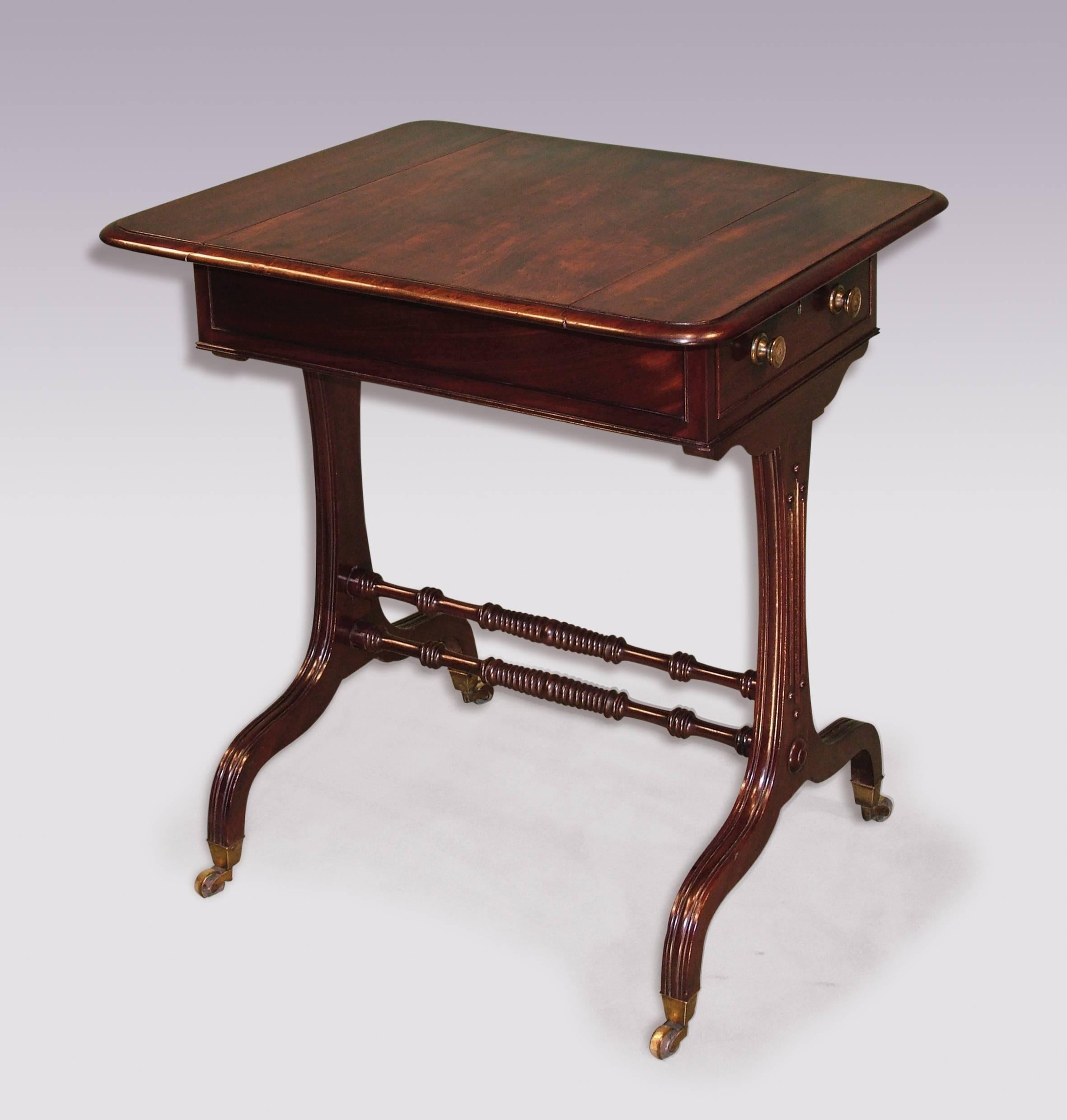 An unusual early 19th century Regency period figured mahogany side table, having moulded edged swivel top, above fitted frieze drawer and reeded umbrella shaped end supports, joined by ring turned stretchers, retaining original brass castors.