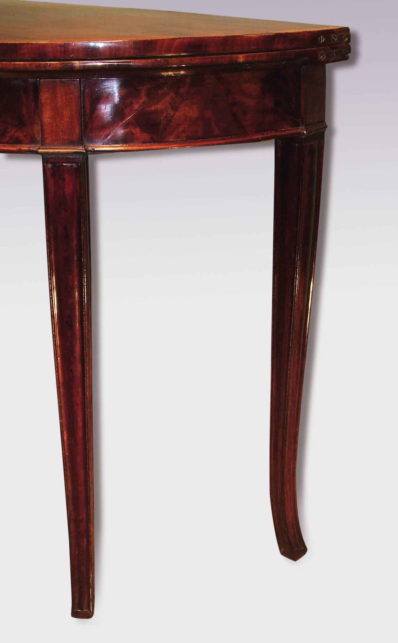 A late 18th century Sheraton period figured mahogany half round card table, of attractive small proportions, having tulipwood crossbanded top above flame figured frieze, supported on fluted outswept tapering legs.