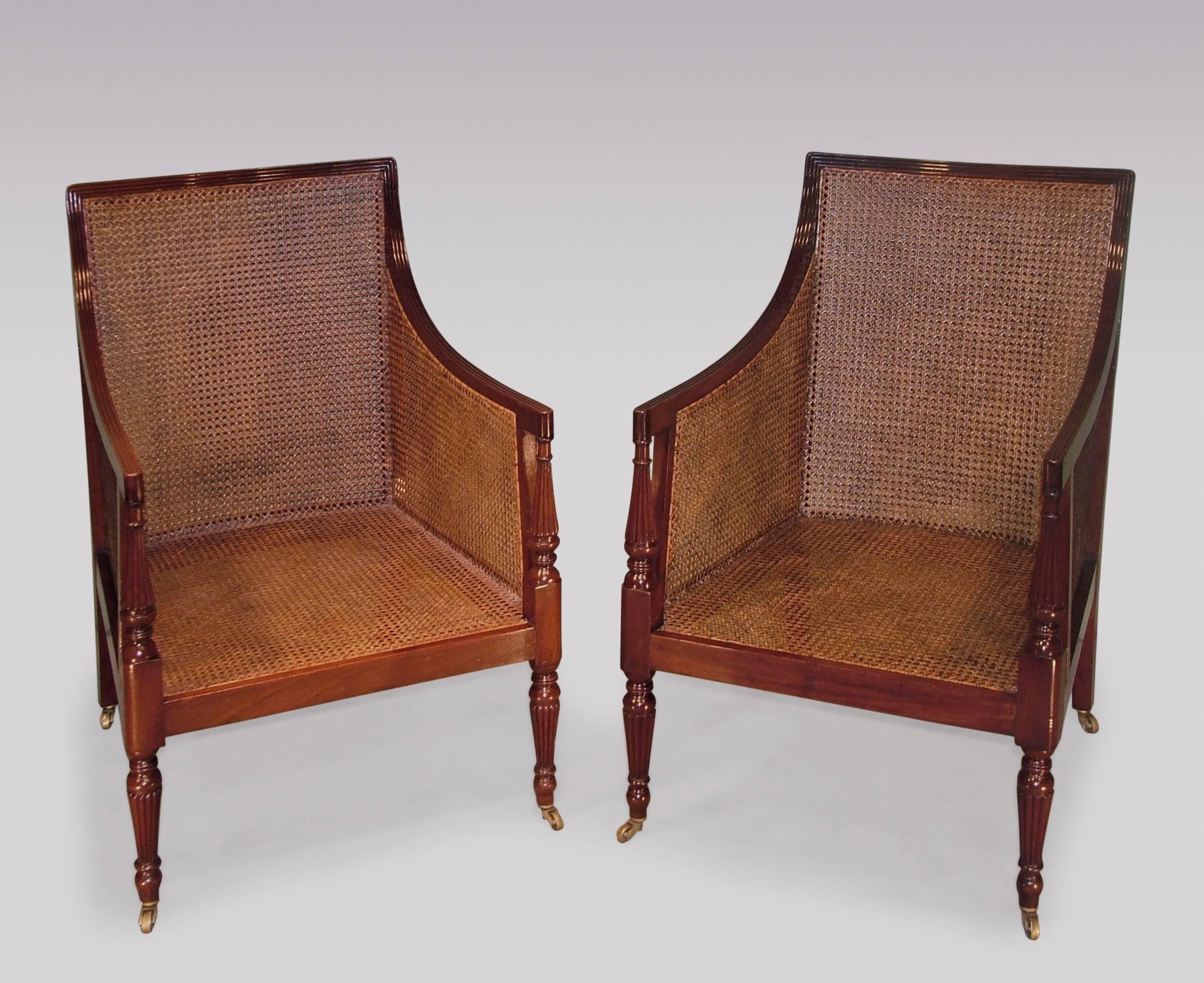 A near pair of early 19th century Regency period mahogany caned library bergere chairs, having receded backs and arms, above turned, tapering and receded arm supports and legs, ending on brass castors.