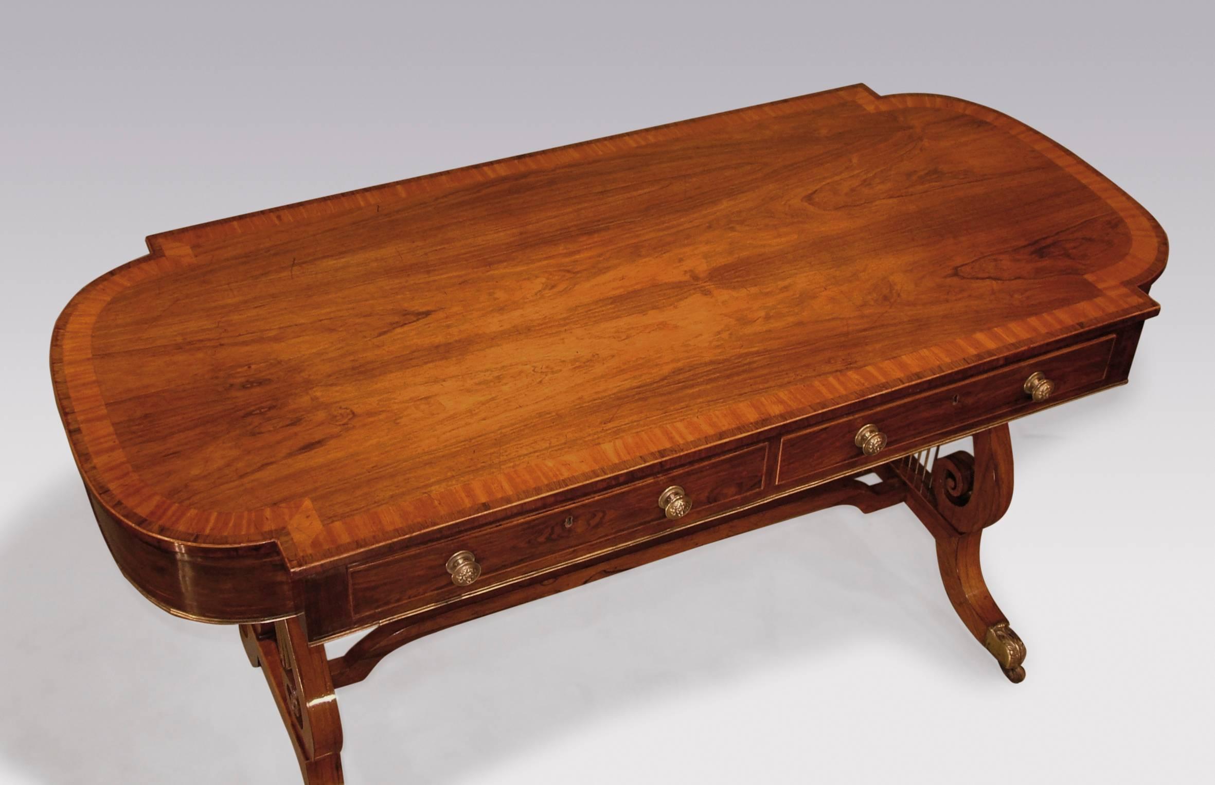 An early 19th century Regency period rosewood writing table, boxwood strung throughout, having lobe ended satinwood crossbanded top, above brass moulded edge frieze. The table with two real and two dummy drawers, raised on lyre end supports joined