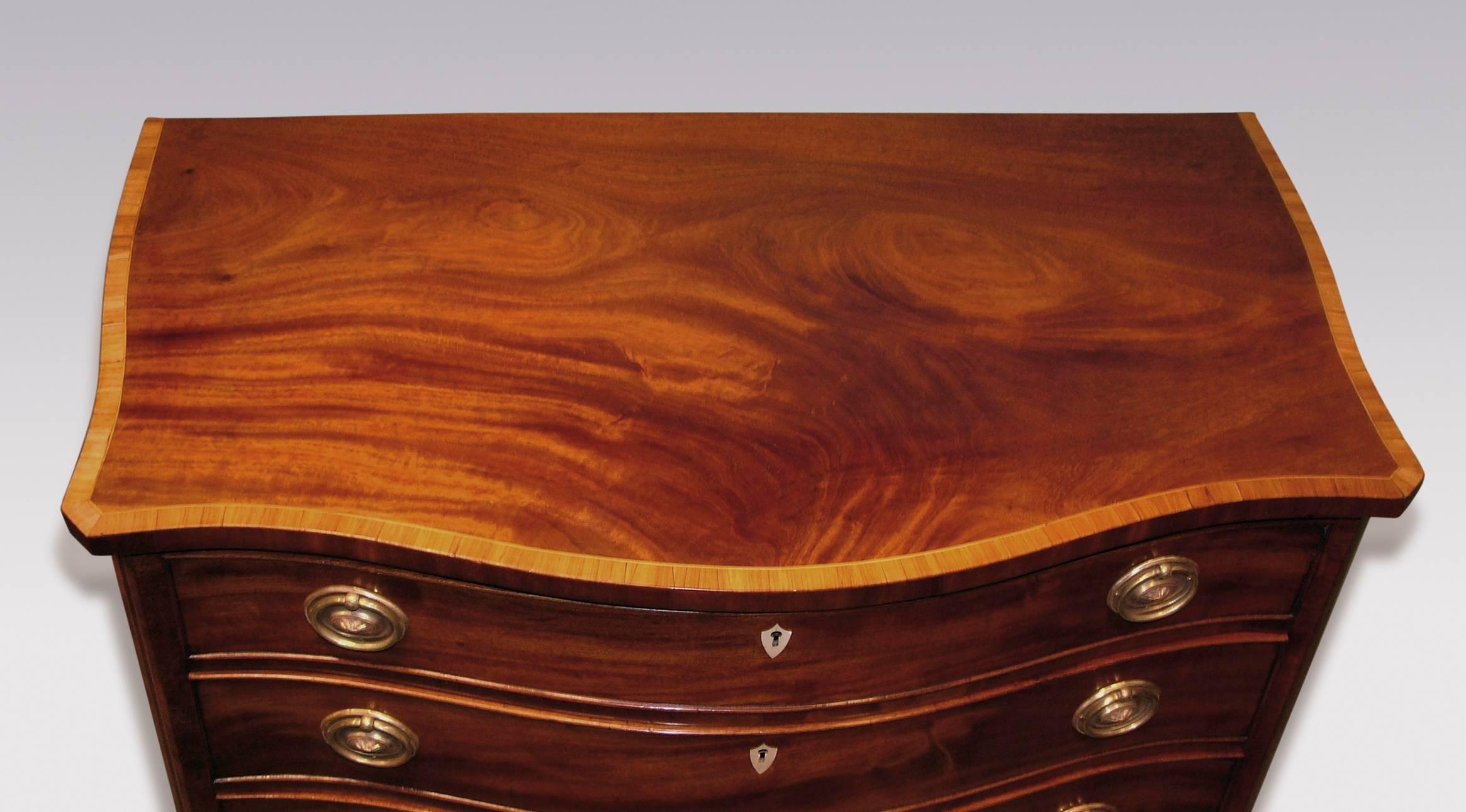 A mid-18th century George III period well figured mahogany serpentine chest, having tulipwood cross banded and boxwood line inlaid canted cornered top, above four graduated cockbeaded drawers, flanked by purple-heart inlaid canted corners with