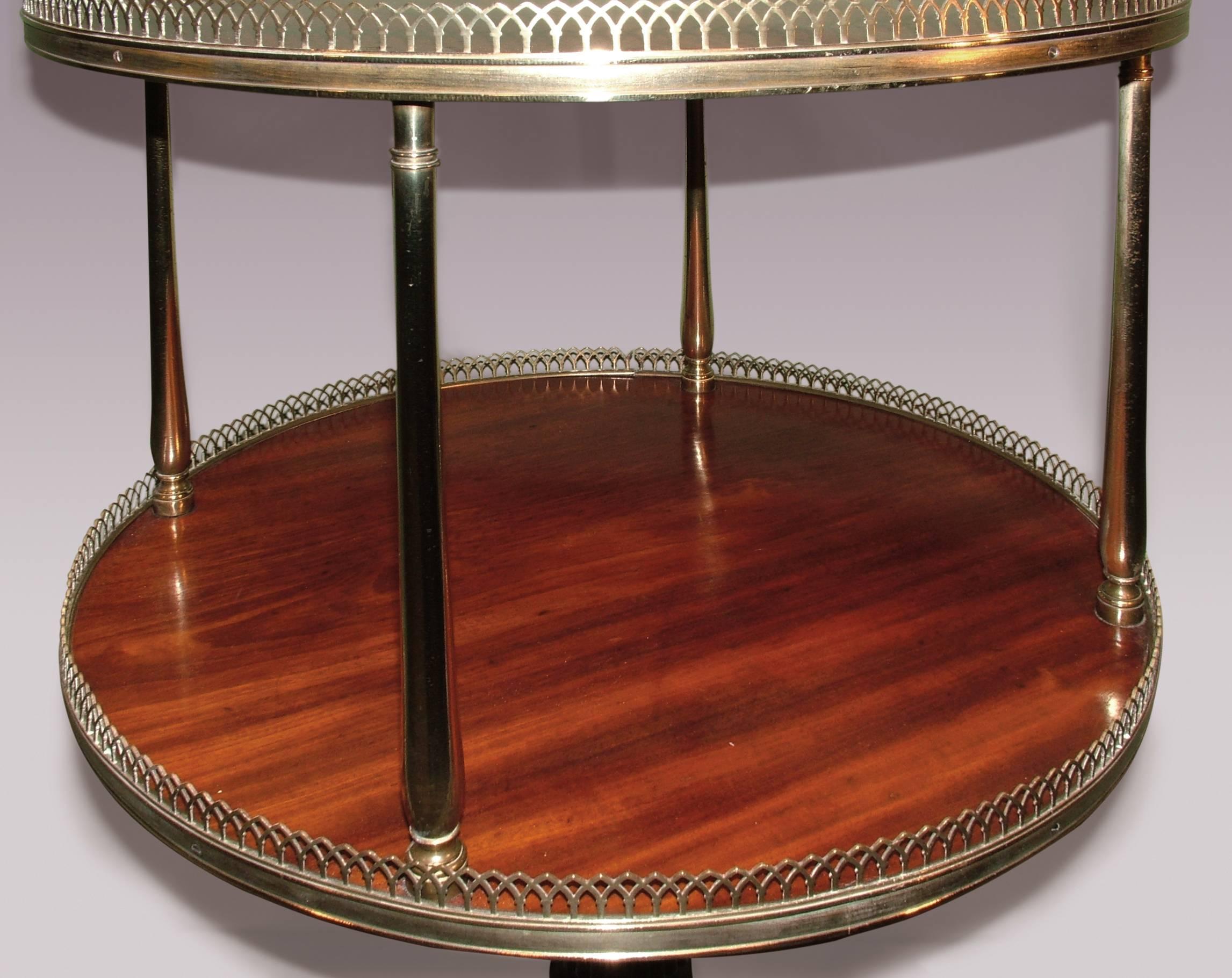 A fine early 19th century Regency period mahogany two-tier circular revolving dumb-waiter having brass gothic-arch galleries and brass baluster-turned supports, raised on reeded column and reeded three-splay legs ending on brass box castors.